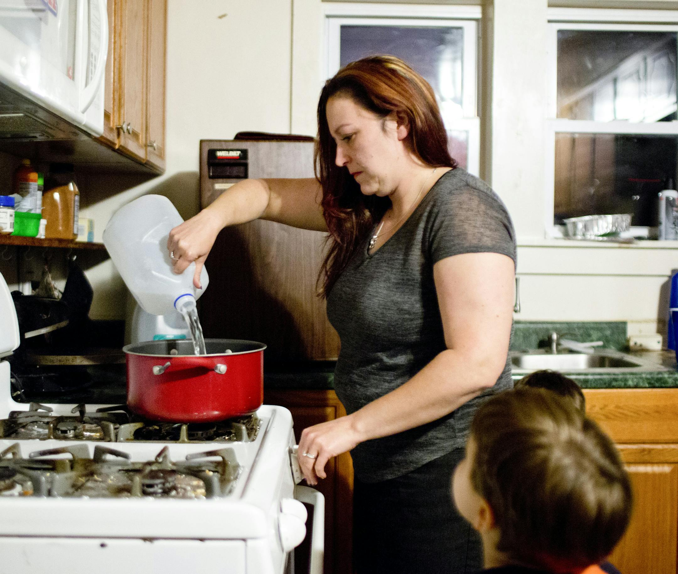 Lee Walters empties a bottle of store-bought drinking water into a pot to make pasta for dinner while her son Gavin, 4, watches at her home in Flint, Mich., Oct. 6, 2015. Walters said test results showed an elevated lead level in his blood after the city switched to water from the Flint River. Contaminated water has become the latest blow to the economically battered city that has struggled for years with factory closings, job losses and population decline. (Laura McDermott/The New York Times)