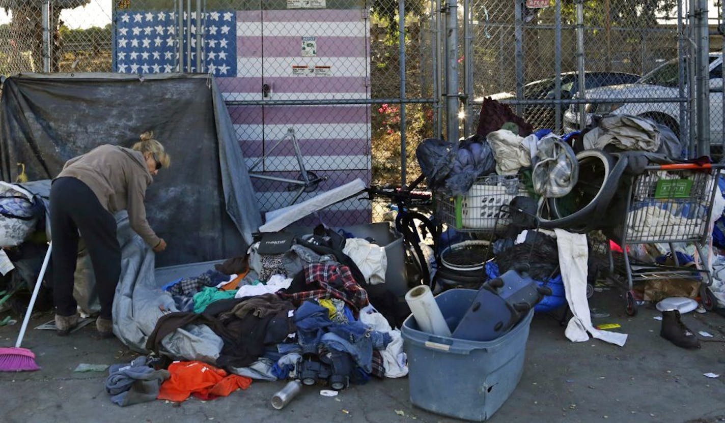 In this Sept. 25, 2017 photo, a woman who was camping in downtown San Diego sorts through her belongings on a sidewalk that was being sprayed with a bleach solution to fight a deadly hepatitis A outbreak. The increased number of hepatitis cases in the homeless population and the geographic spread of the disease led California to declare a state of emergency in October.