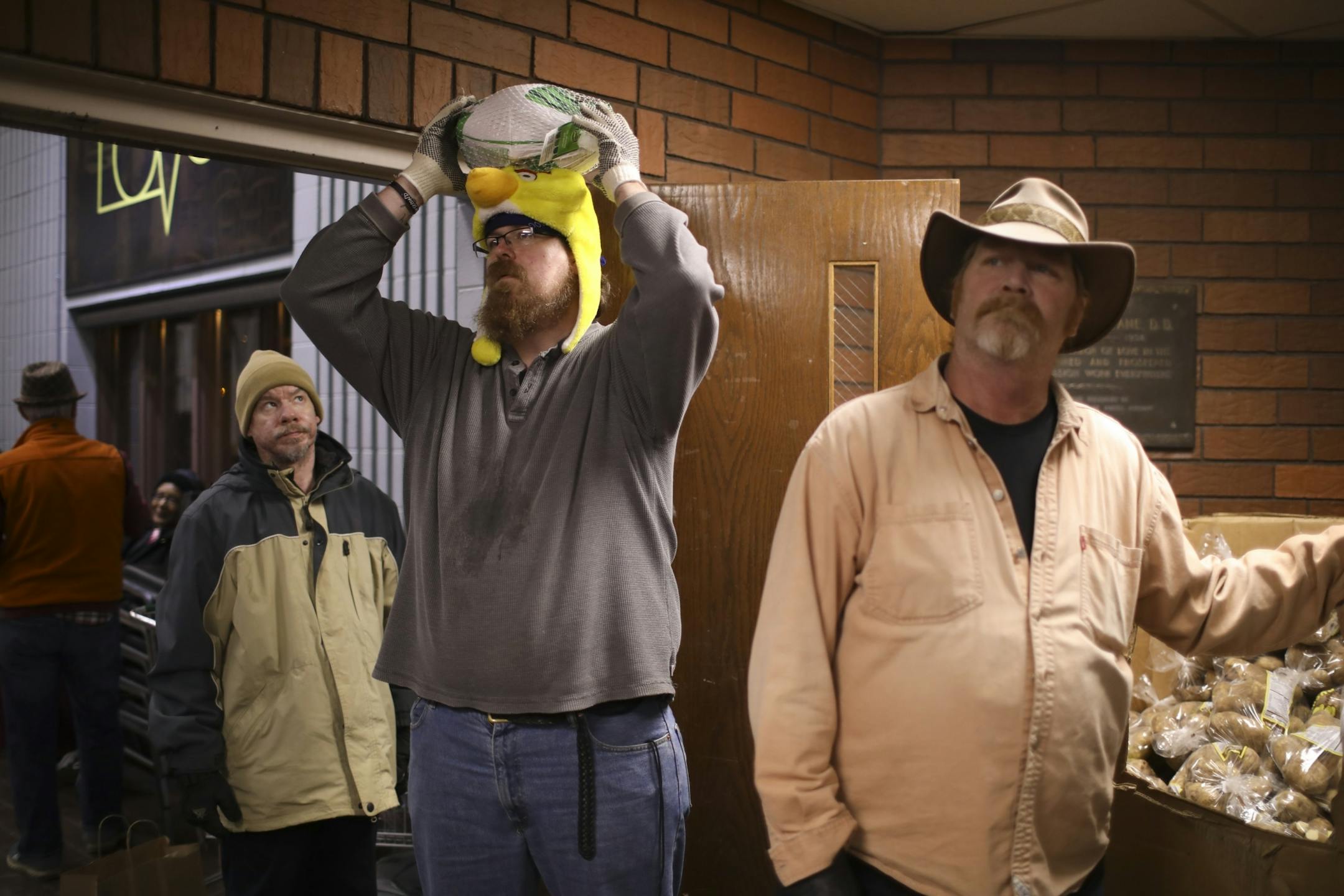 Mark Peterson looked up at Bob Holzemer as he tried balancing a turkey on his head. They were volunteers waiting in line with Rich Smith, right, poised to help carry Thanksgiving meal packages out to people's cars Monday night at the Union Gospel Mission in St. Paul.
