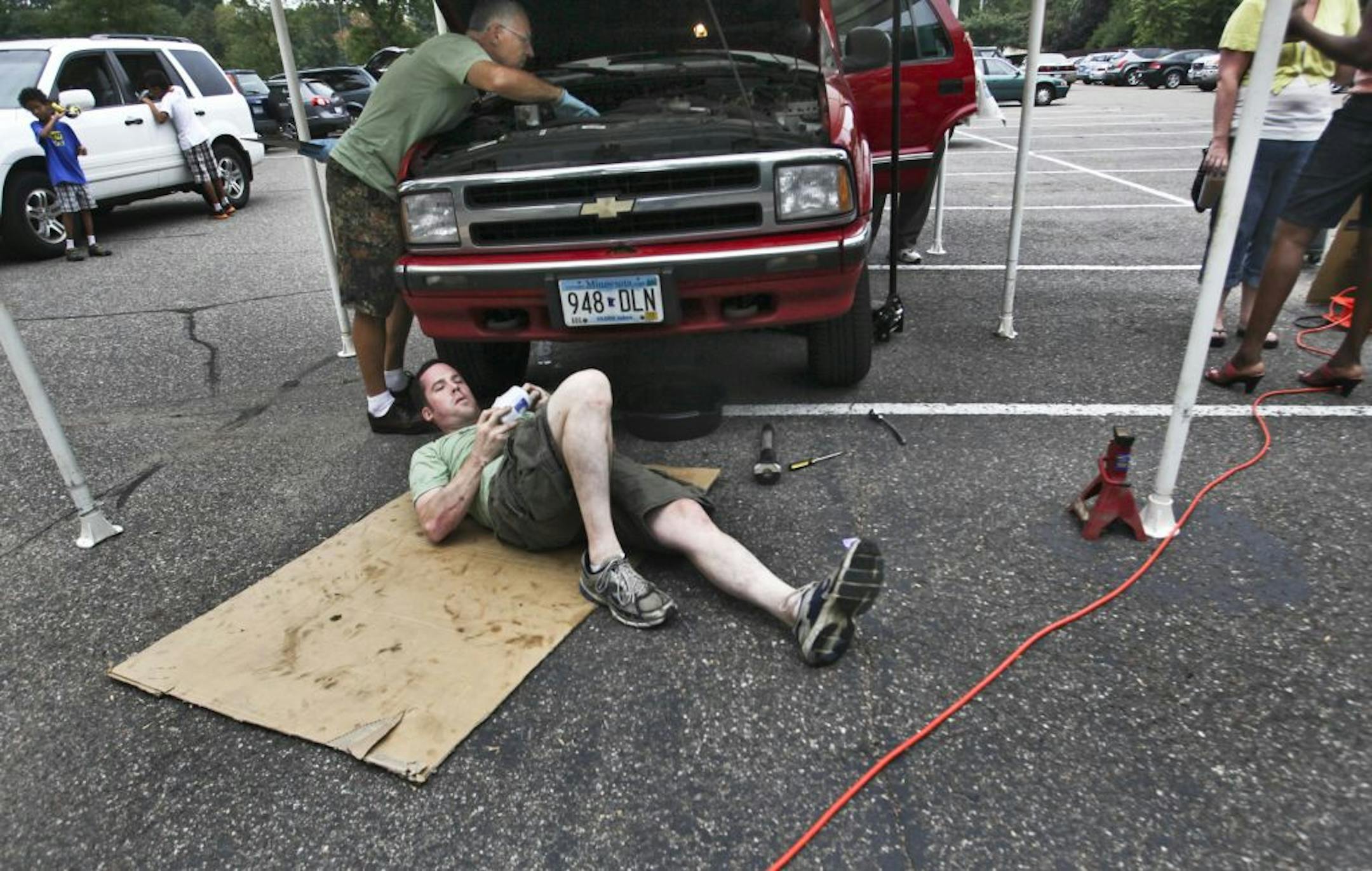 Evangelical church volunteers Dean Marshall, middle rear, and Adam DeGroff, middle front, work on changing the oil and doing other general maintenance to a 1996 Chevy Blazer owned by a single parent and getting serviced for free as a part of CityServe Saturday, Aug. 25, 2012, at Evergreen Church in Bloomington, MNl.
