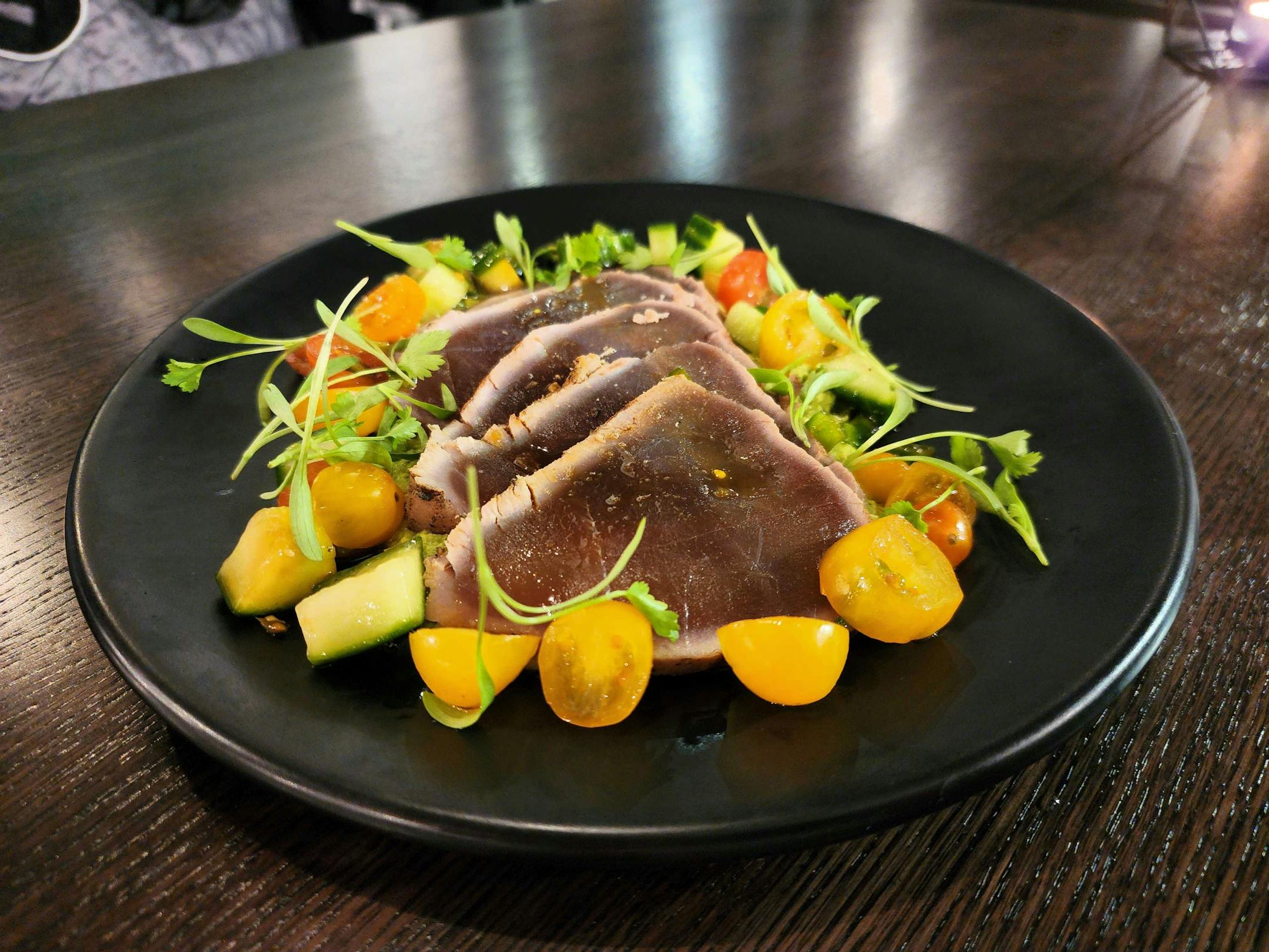 a black plate with triangular slices of seared tuna, surrounded by tomatoes and greens