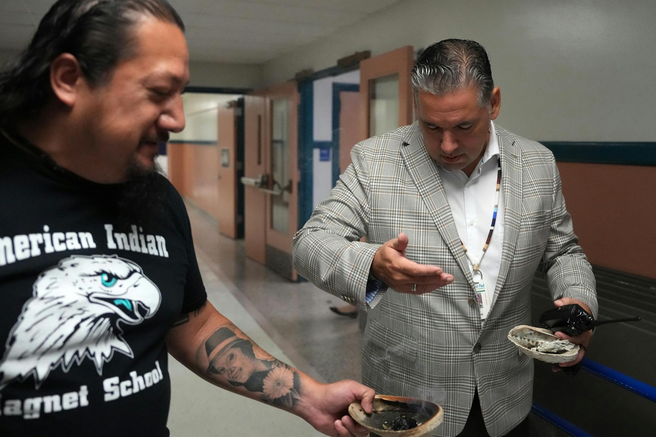 Thomas Draskovic, the kindergarten through fourth grade Lakota language and culture specialist at the American Indian Magnet School, stops at principal Timothy Brown as he walks through the halls as he smudges the school on the first day of class.
