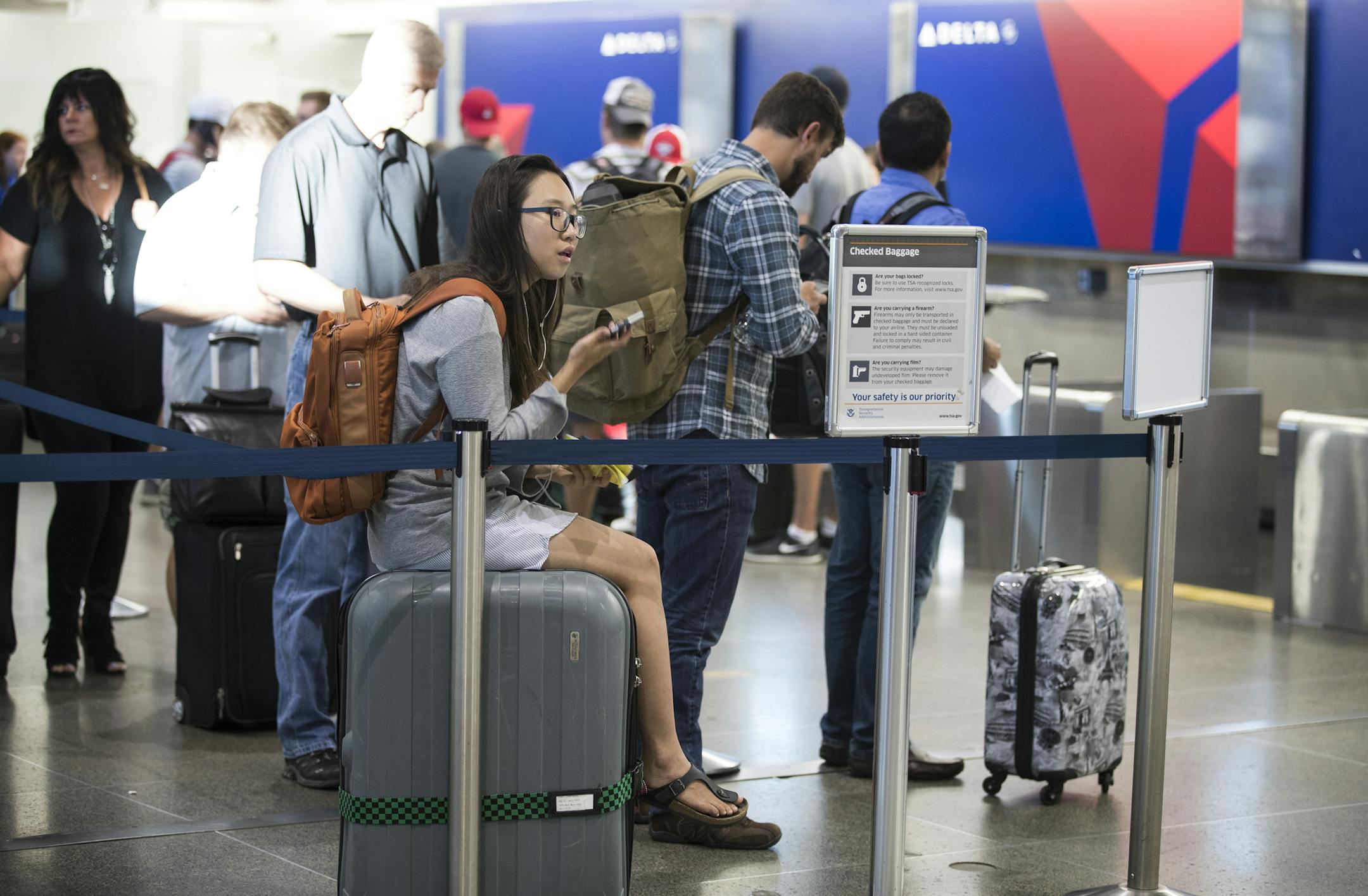 A woman sits on her luggage as she waited in line Monday, Aug. 8, 2016, at the Delta check in area at MSP Airport.