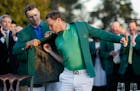 Defending champion Jordan Spieth, left, helps 2016 Masters champion Danny Willett, of England, put on his green jacket following the final round of th