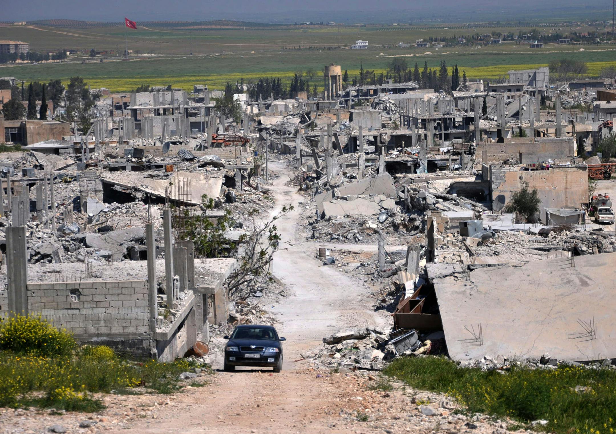 In this picture taken on Saturday, April 18, 2015, a car passes in an area that was destroyed during the battle between the U.S. backed Kurdish forces and the Islamic State fighters, in Kobani, north Syria.