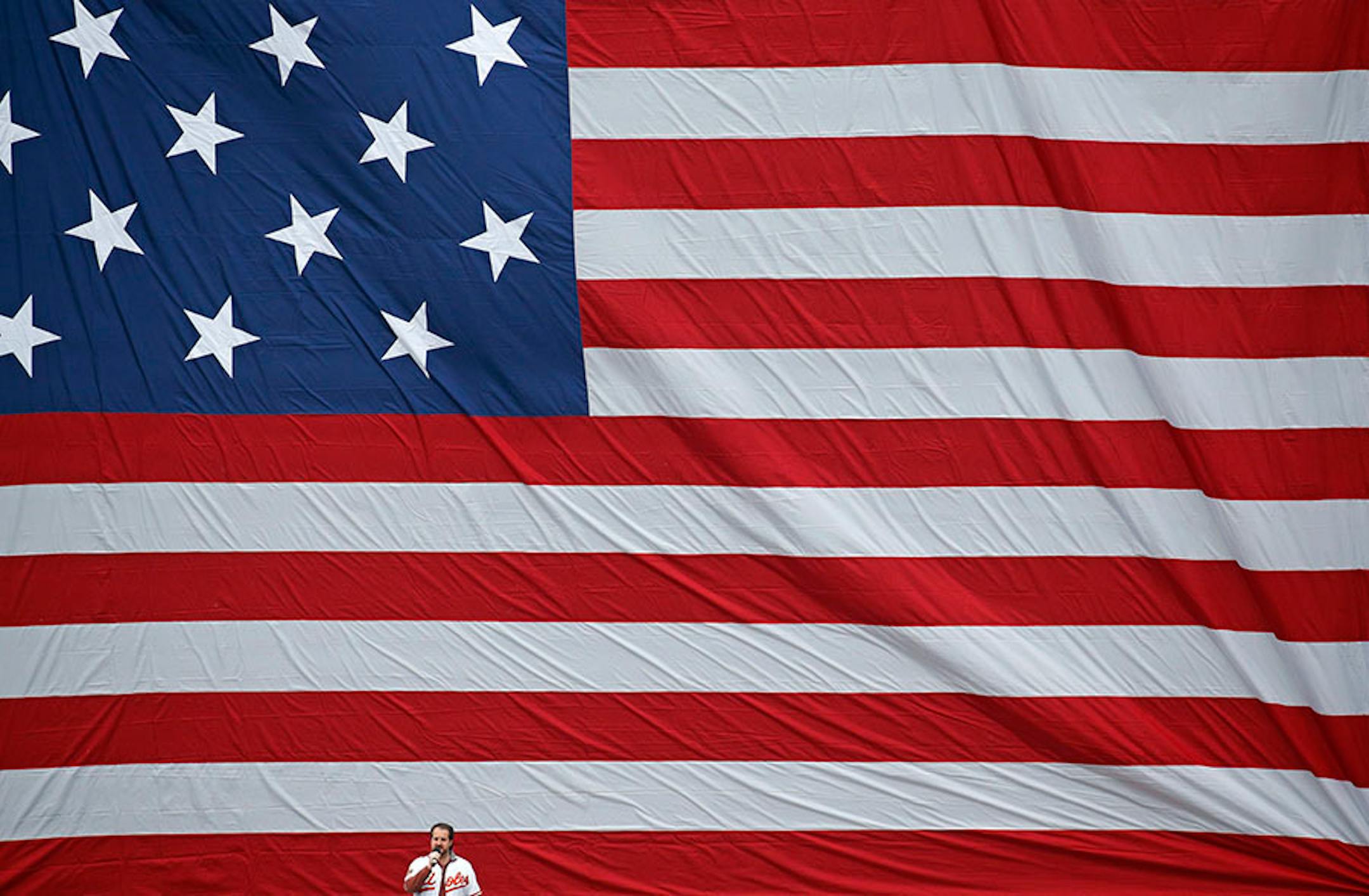 Rolando Sanz sings a rendition of the national anthem in front of a giant American flag before an opening day baseball game between the Baltimore Orioles and the Minnesota Twins in Baltimore, Monday, April 4, 2016. (AP Photo/Patrick Semansky)