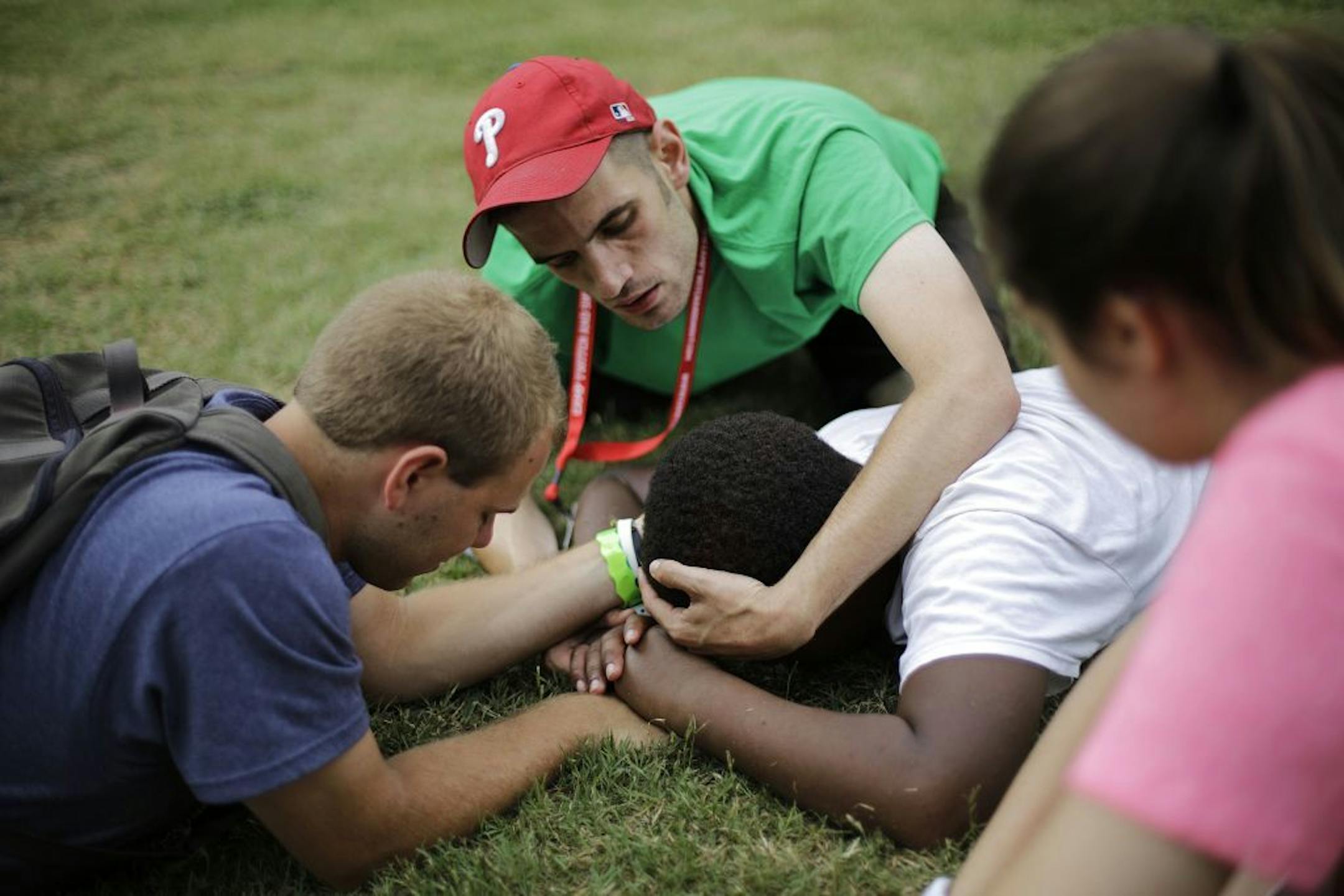 In this July 15, 2014 photo, counselors Paul Luongo, 24, from left, Louis Centanni, 28, and Alex Berthelot, 19, hold the head and hands of camper Lazarus Jordan, 13, of Long Beach, Calif., to prevent him from hurting himself as he experiences a tic where he suddenly drops to the ground and hits the grass with his head and hands while playing the game "capture the flag" with fellow campers at Camp Twitch and Shout, a camp for children with Tourette Syndrome in Winder, Ga. The children�s tics rang