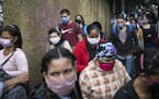 Pedestrians and commuters wearing face masks amid the new coronavirus pandemic crowd a sidewalk near a bus stop in Caracas, Venezuela, Monday, June 1,