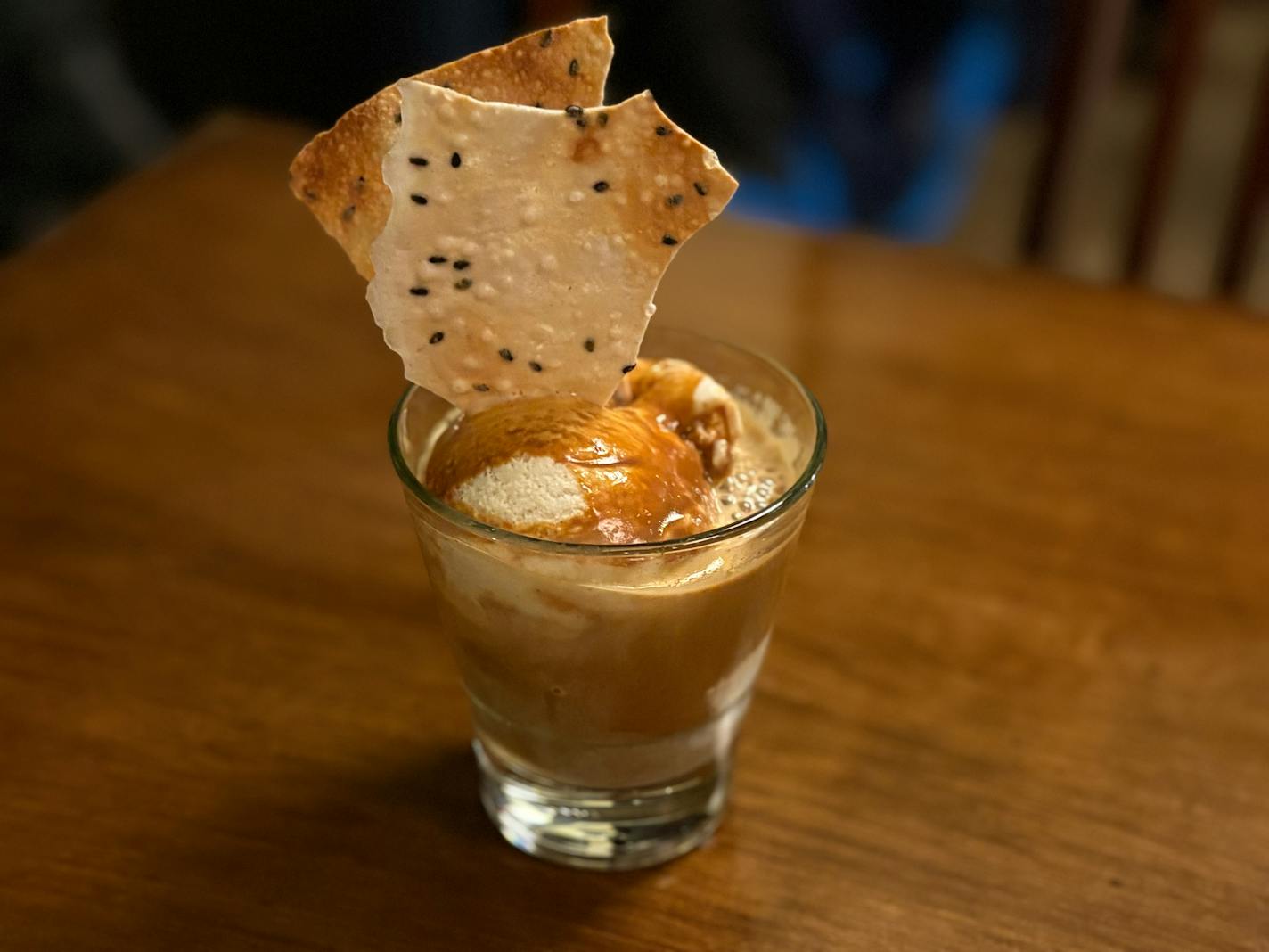 A low glass sports a scoop of condensed milk flavored ice cream, covered in espresso and sporting a sesame seed dotted twille