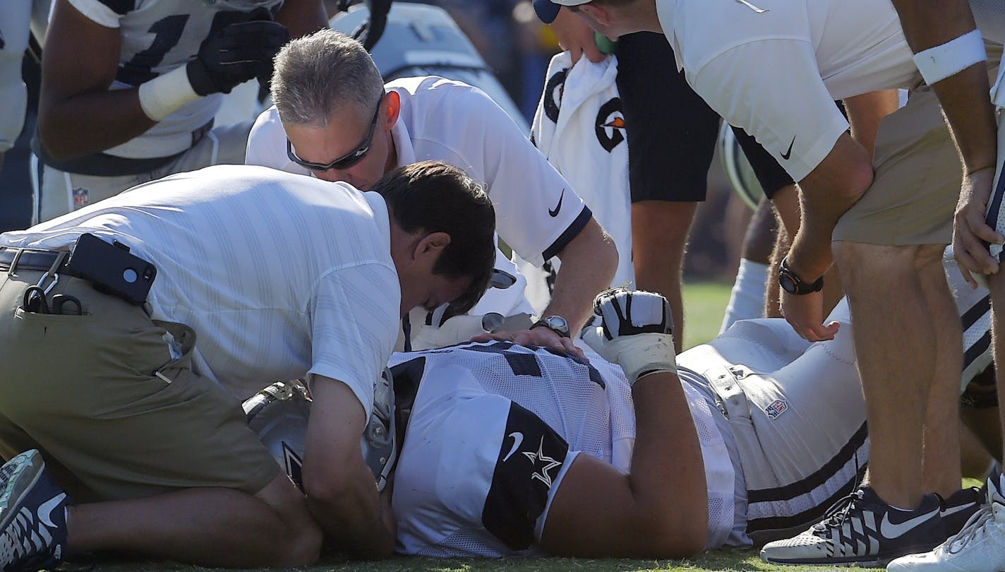 Dallas Cowboys guard Zack Martin is tended to after being injured as wide receiver Devin Street, left, and quarterback Tony Romo, right, stand by during a joint NFL football training camp with the St. Louis Rams, Tuesday, Aug. 18, 2015, in Oxnard, Calif. (AP Photo/Mark J. Terrill)