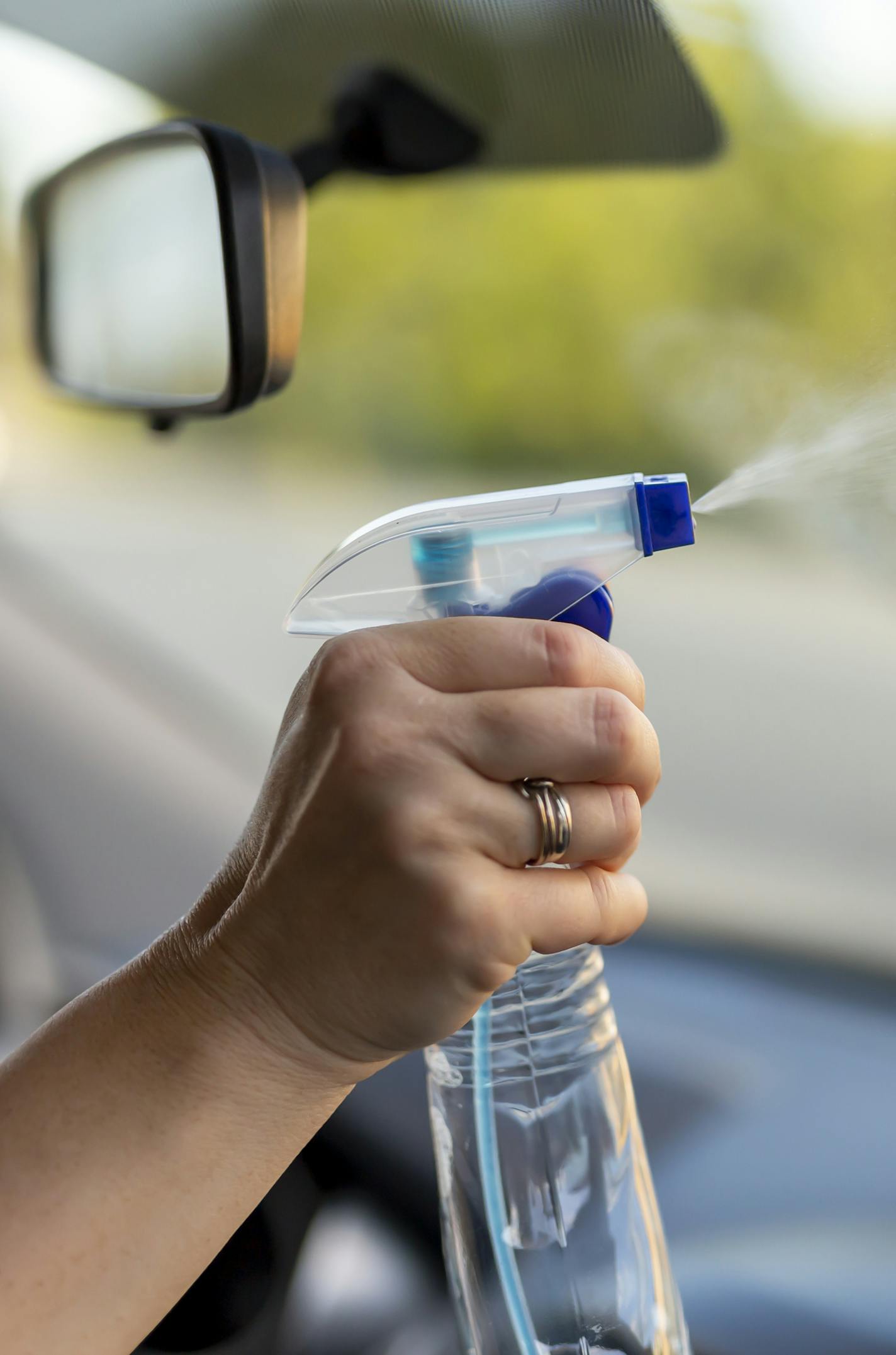 Detail of female hand cleaning a car windshield while washing car with cleanser spray