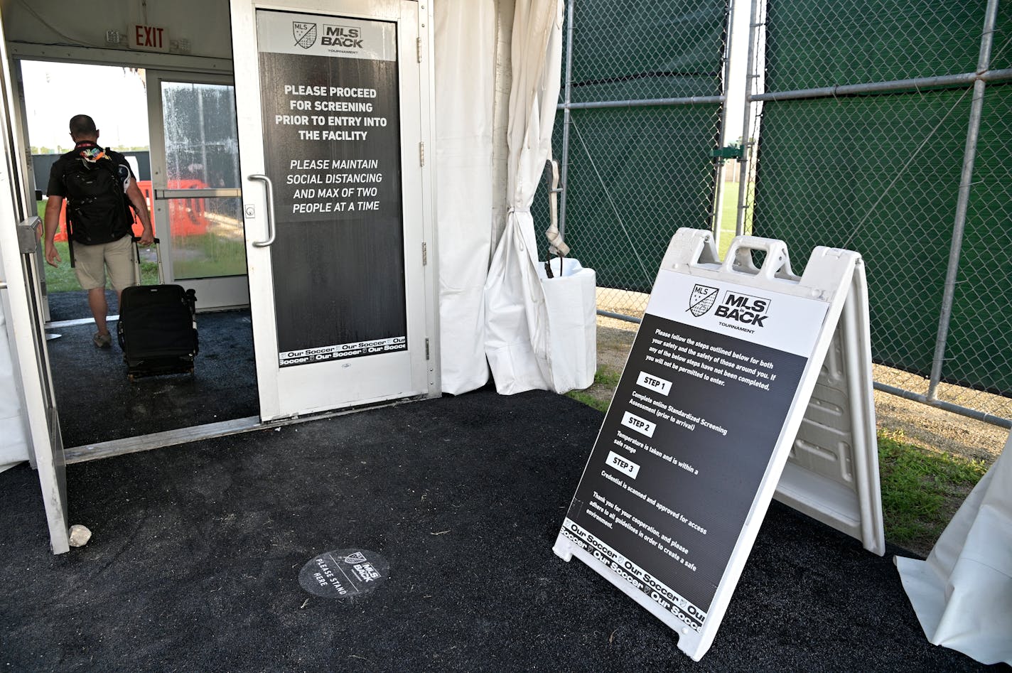 A member of the media walks through a health-screening checkpoint at a security entrance to the ESPN Wide World of Sports complex before an MLS soccer match between the Philadelphia Union and New York City FC, Thursday, July 9, 2020, in Kissimmee, Fla. (AP Photo/Phelan M. Ebenhack)