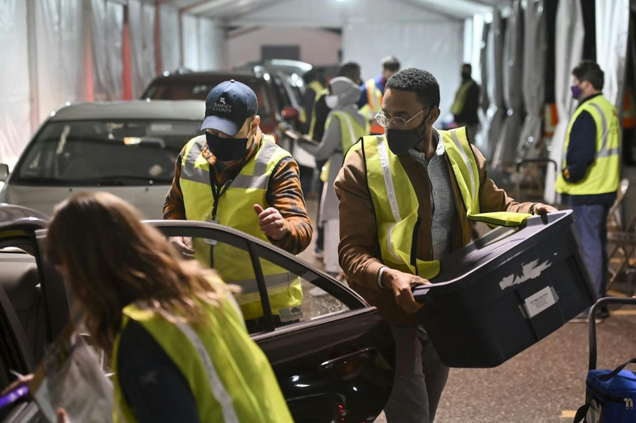 Carlos Remigio, right, a volunteer, and Michael Lindsay, left of center, a Ramsey County employee, worked to unload the car of an election judge, collecting sealed ballot boxes and voting equipment.