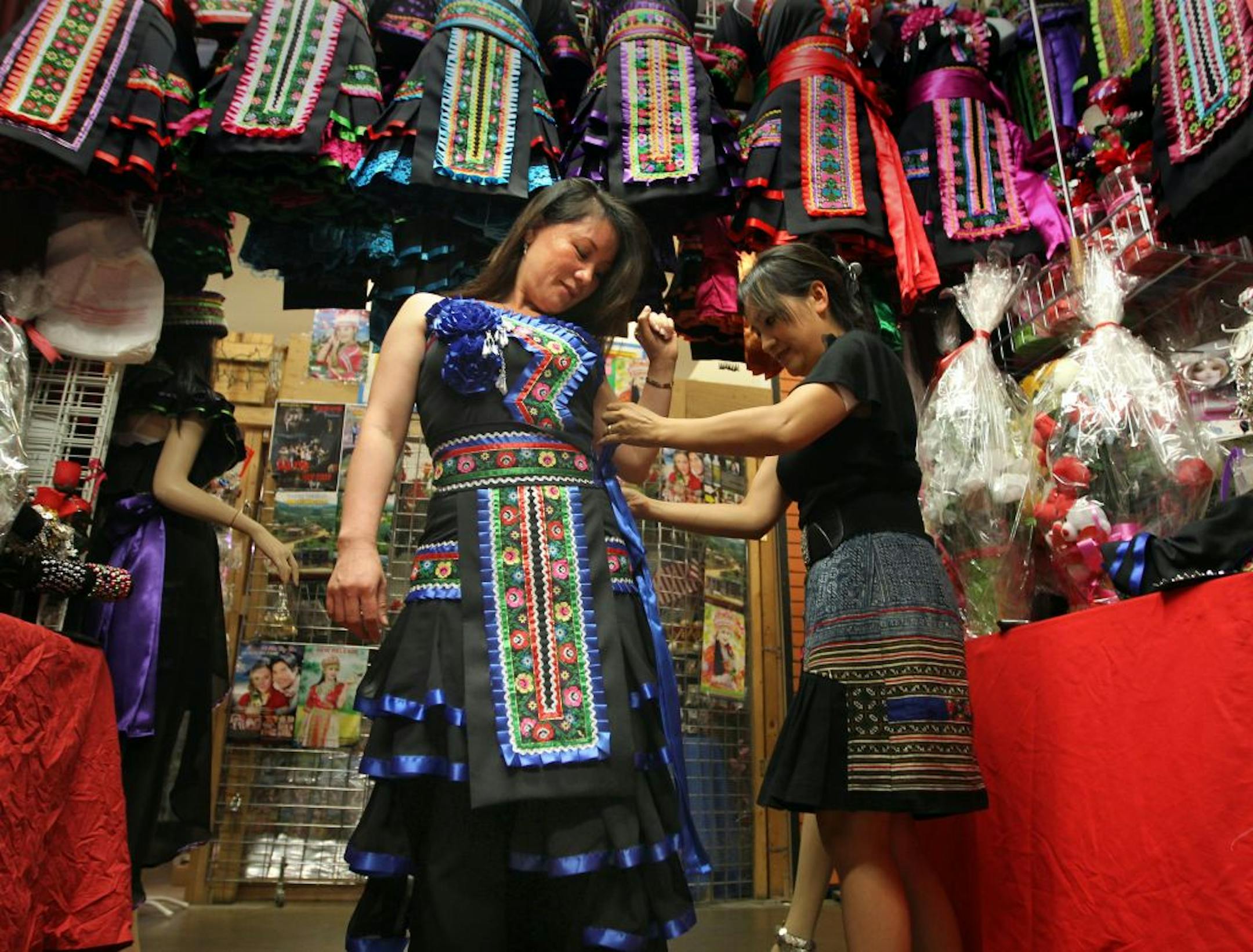Karen Vang tried on a traditional New Year's dress with the help of its maker, Fuzhen Yang, in her shop at Hmongtown Marketplace in St. Paul.