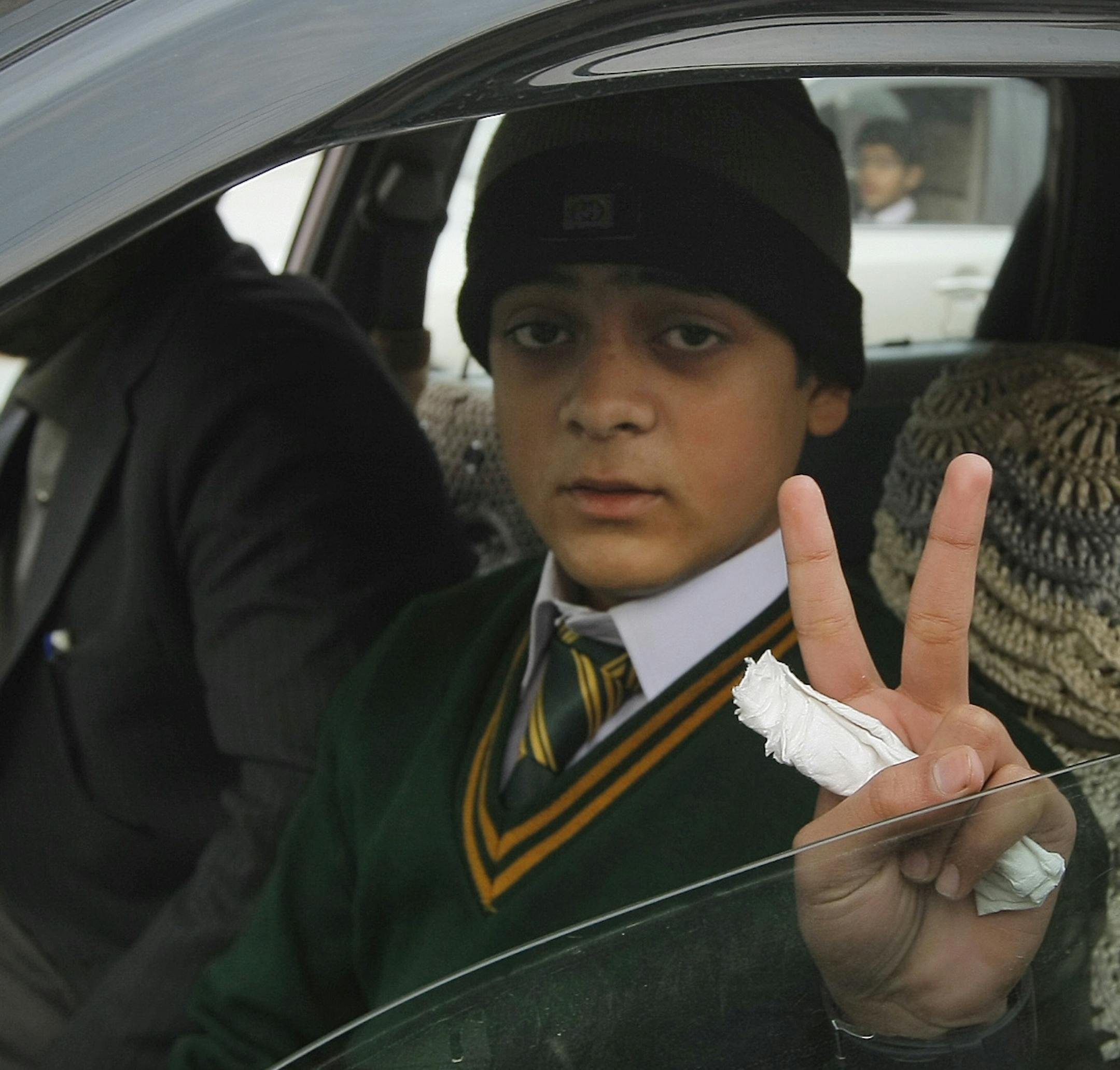 Mohammad Baqair, who survived last month's Taliban attack on a military-run school that killed his mother, flashes a victory sign on his way to the Army Public School which was targeted by Taliban militants, in Peshawar, Pakistan, Monday, Jan. 12, 2015. Pakistani children and staff were returning to a school in northwestern Pakistan where Taliban gunmen nearly a month ago killed 150 people — almost all of them students.(AP Photo/Mohammad Sajjad)
