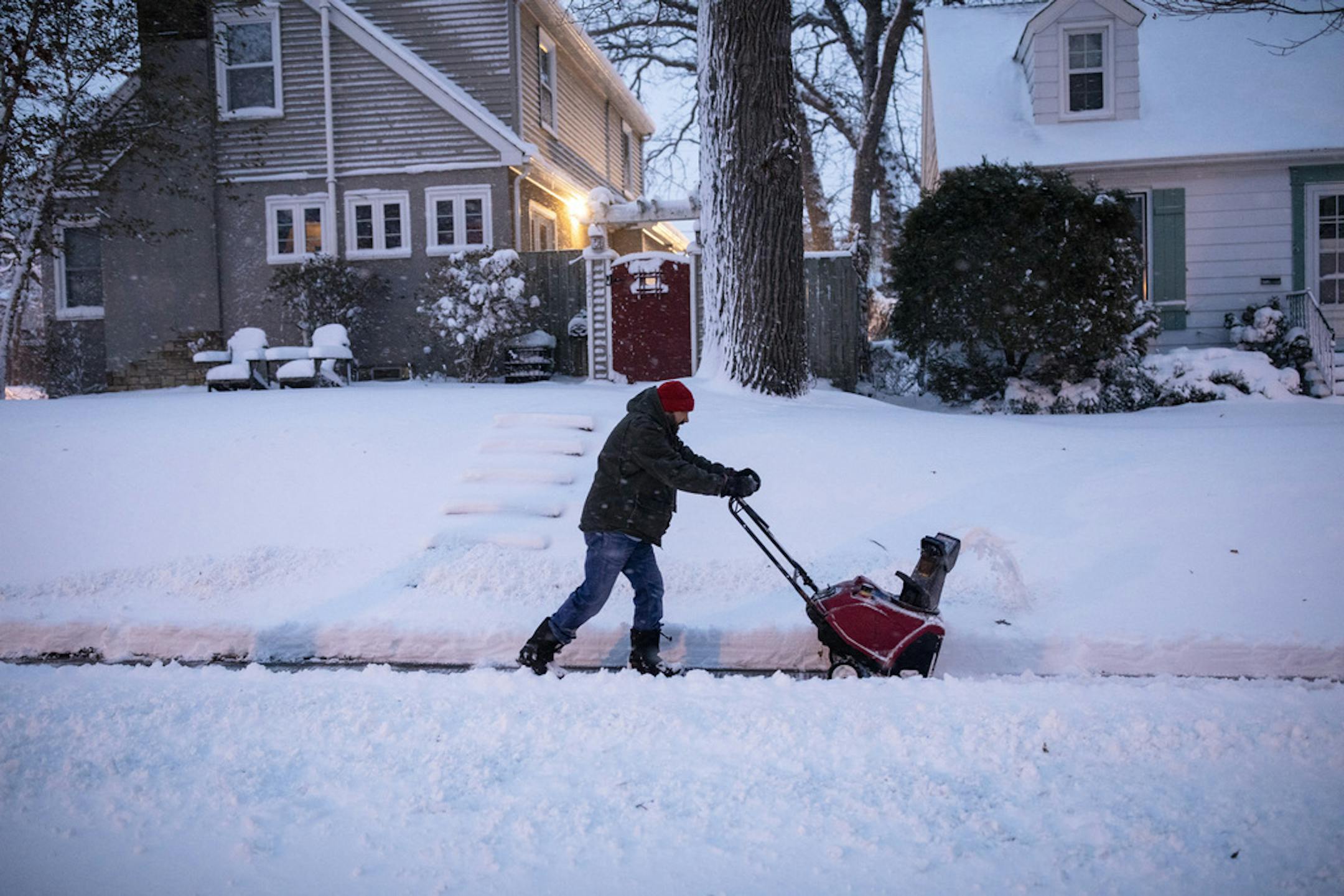 A resident clears snow from the sidewalk outside his home early on Wednesday in Minneapolis, Nov. 27, 2019. A winter storm that barreled across the United States from Cedar Grove, Calif., where it dropped 49 inches of snow, to Ogunquit, Maine, which saw more than a foot, was finally departing on Tuesday, but not before giving New England one last whack. (Tim Gruber/The New York Times)