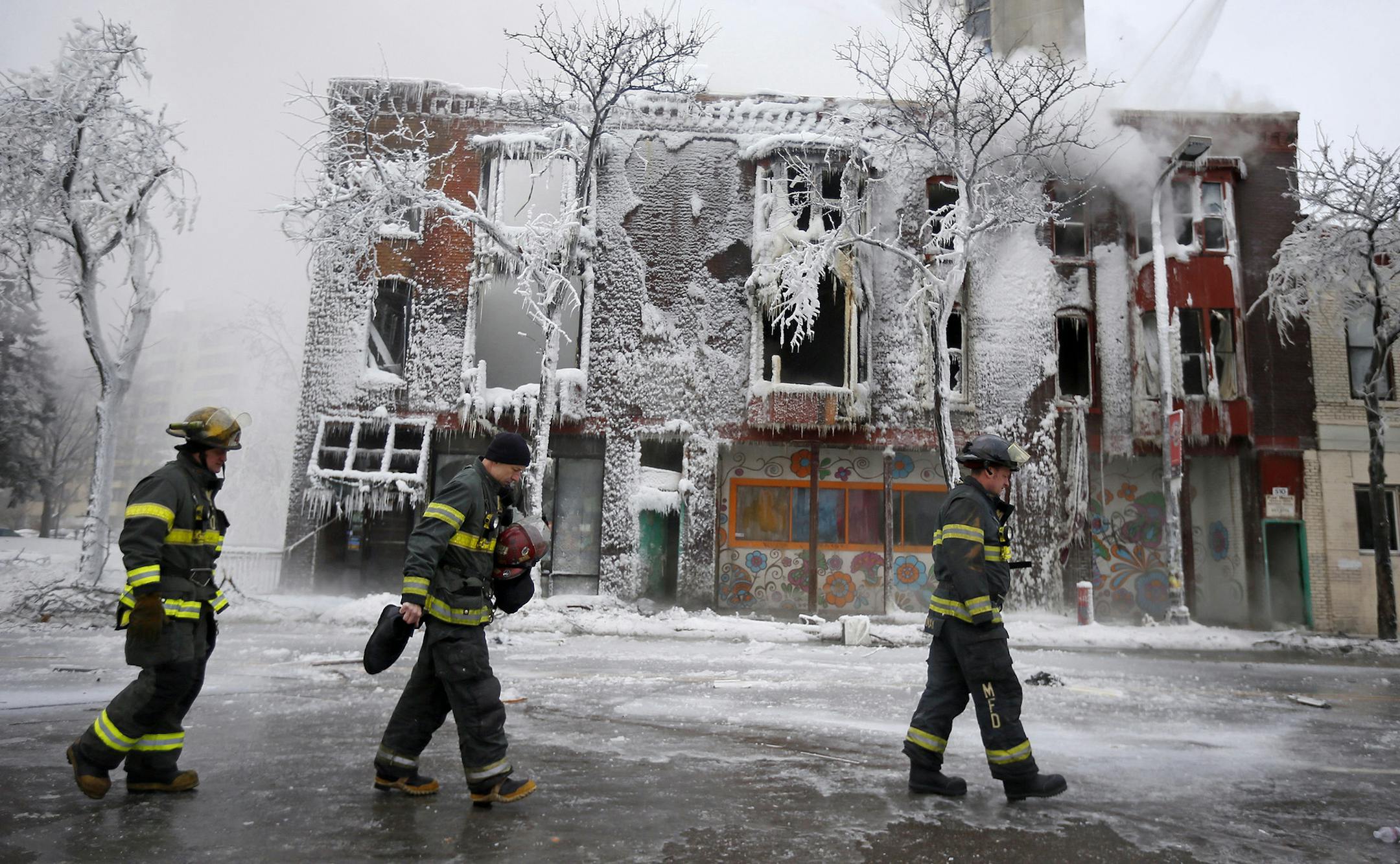 Fire fighters walked in front of a building after a fire an explosion at 514 Cedar Avenue January 01, 2014 in Minneapolis. Thirteen people were injured, six critically, early Wednesday morning after an explosion caused a major fire at a grocery store and apartment building in the bustling Cedar-Riverside neighborhood