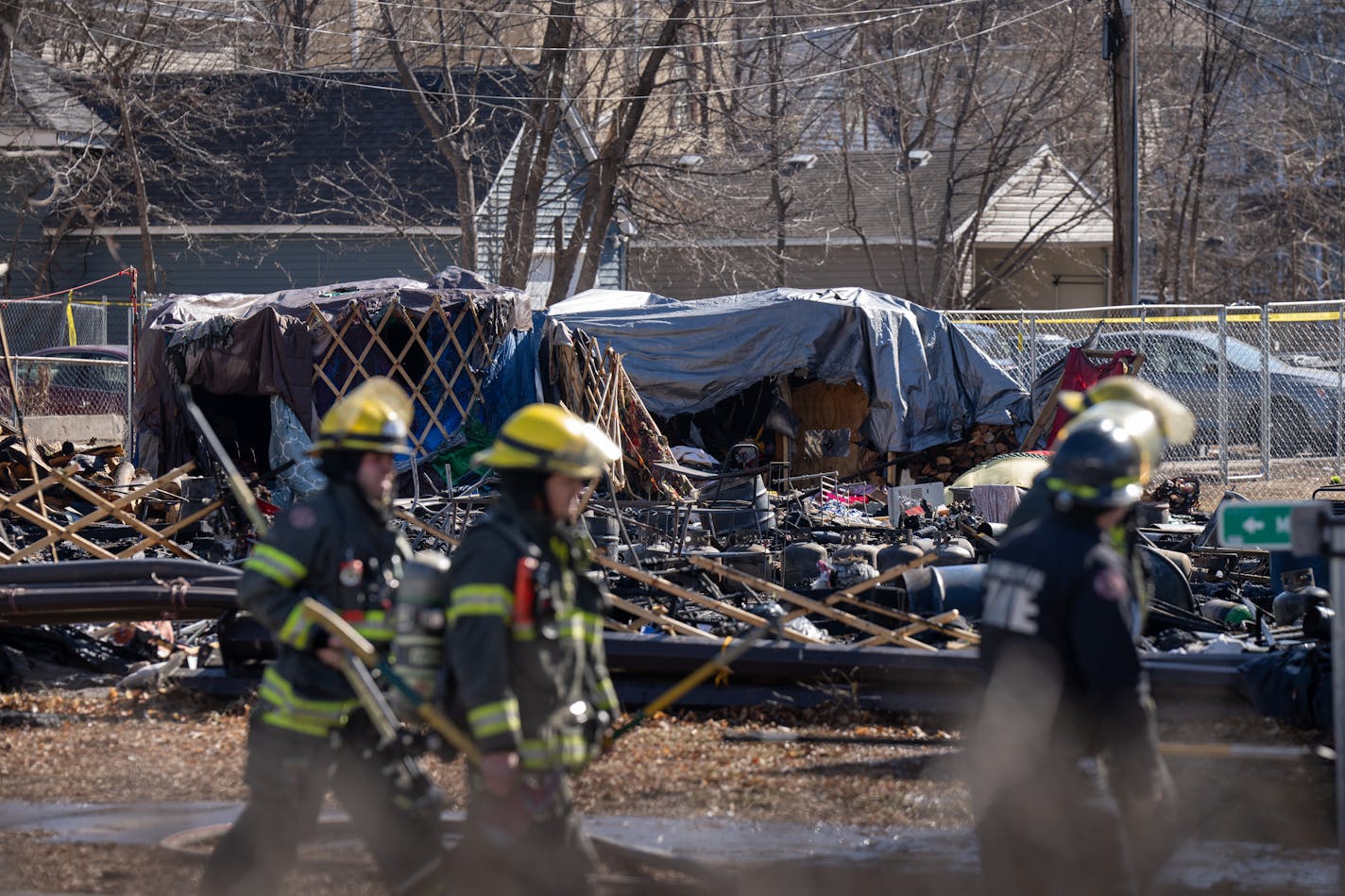 one firefighter walks a few paces ahead of a pair of his colleagues against the backdrop of burnt debris and makeshift tents