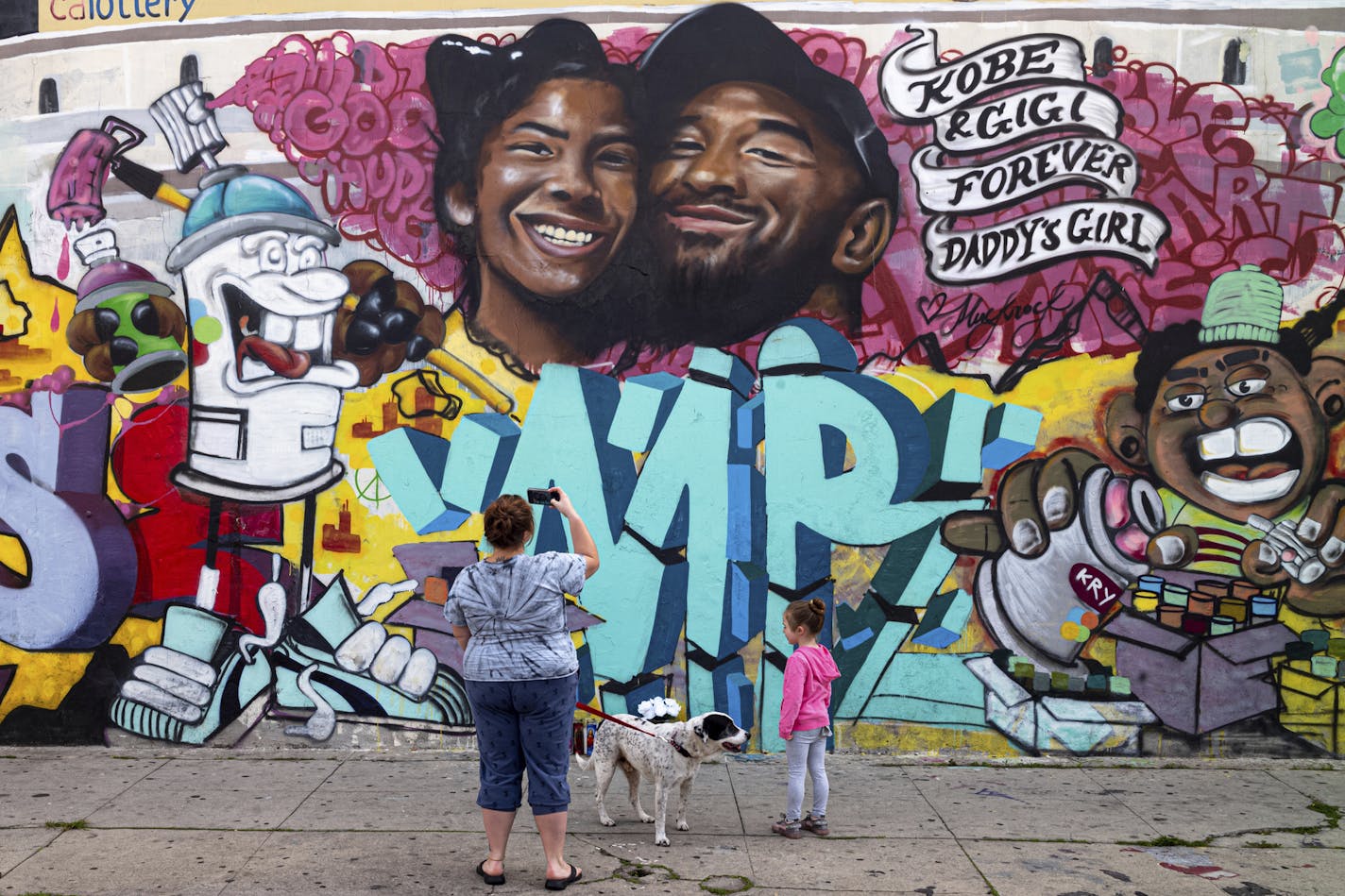 Bryan Esparaza and her daughter Amelia, 4, pause in front of a mural put up of Kobe Bryant and his daughter along Pickford Street in Los Angeles, Monday, Jan. 27, 2020. Bryant, the 18-time NBA All-Star who won five championships and became one of the greatest basketball players of his generation during a 20-year career with the Los Angeles Lakers, died in a helicopter crash Sunday. (David Crane/The Orange County Register via AP)