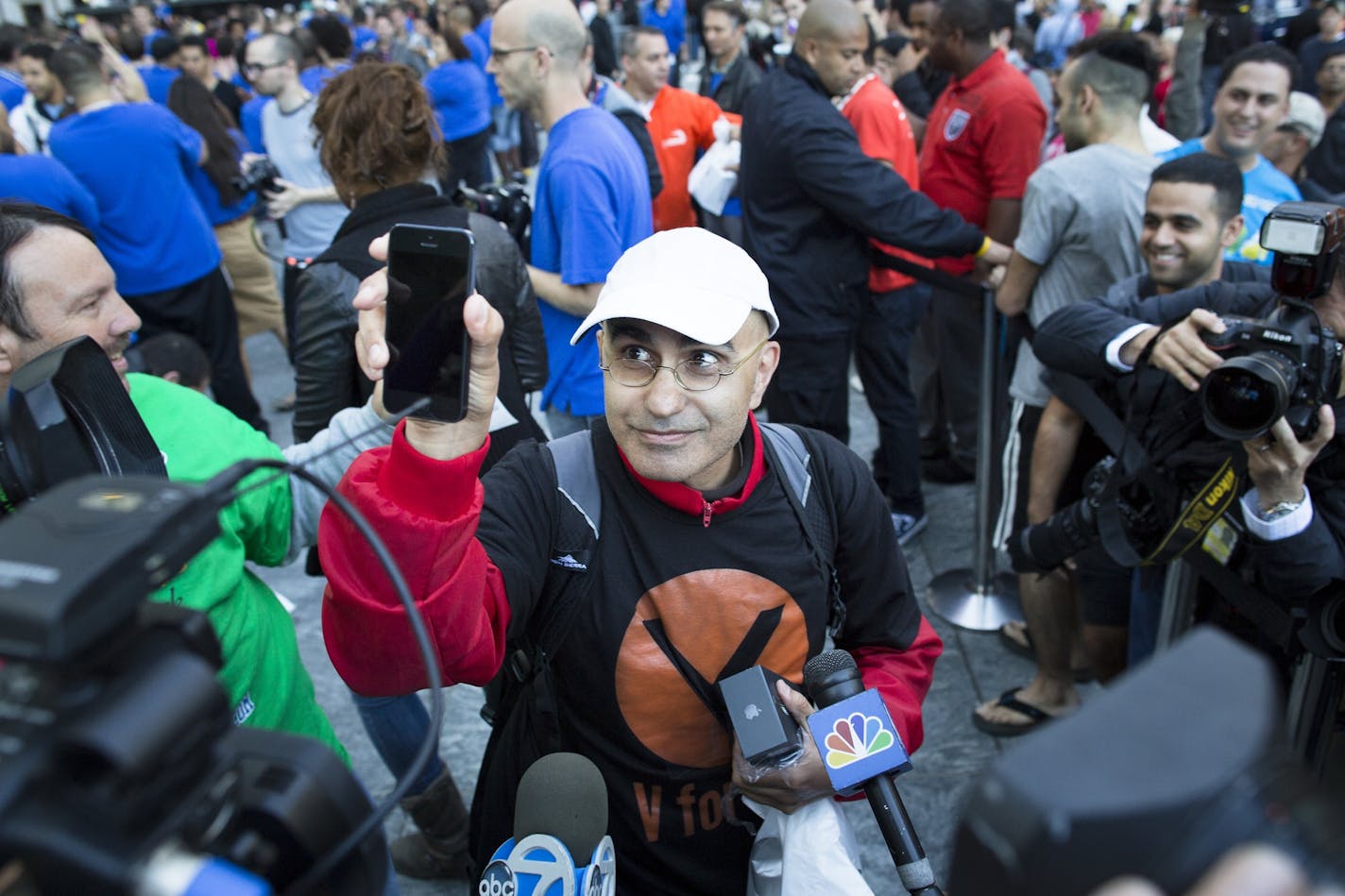 Hazem Sayed, 54, the first in line to purchase the new iPhone 5, holds up his new phone in front of media outside the Fifth Avenue Apple store, Friday, Sept. 21, 2012, in New York. Hundreds of people waited in line through the early morning to be among the first to get their hands on the highly anticipated phone.