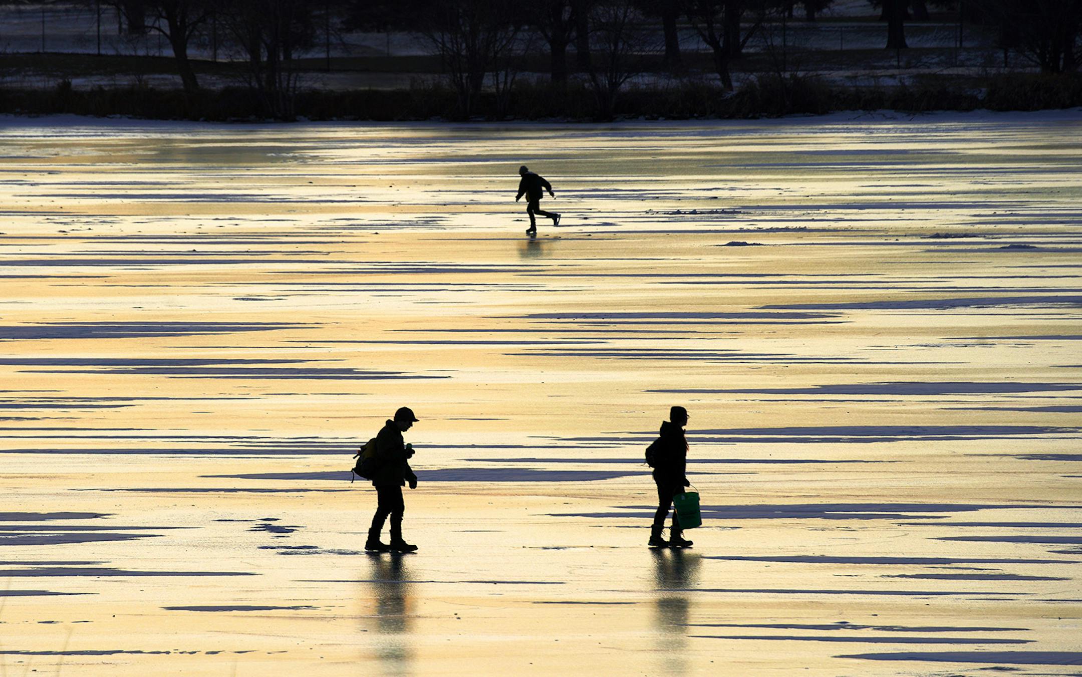 On Lake Hiawatha, an ice fishing couple searches for a good spot while a skater glides across the smooth ice.