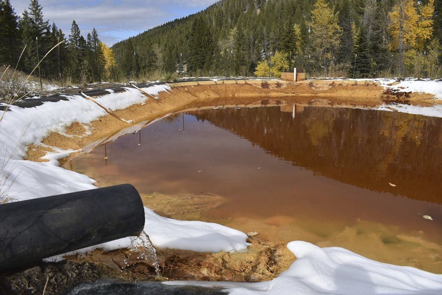 In this Oct. 12, 2018 photo, water contaminated with arsenic, lead and zinc flows from a pipe out of the Lee Mountain mine and into a holding pond near Rimini, Mont. The community is part of the Upper Tenmile Creek Superfund site, where dozens of abandoned mines have left water supplies polluted and residents must use bottled water.