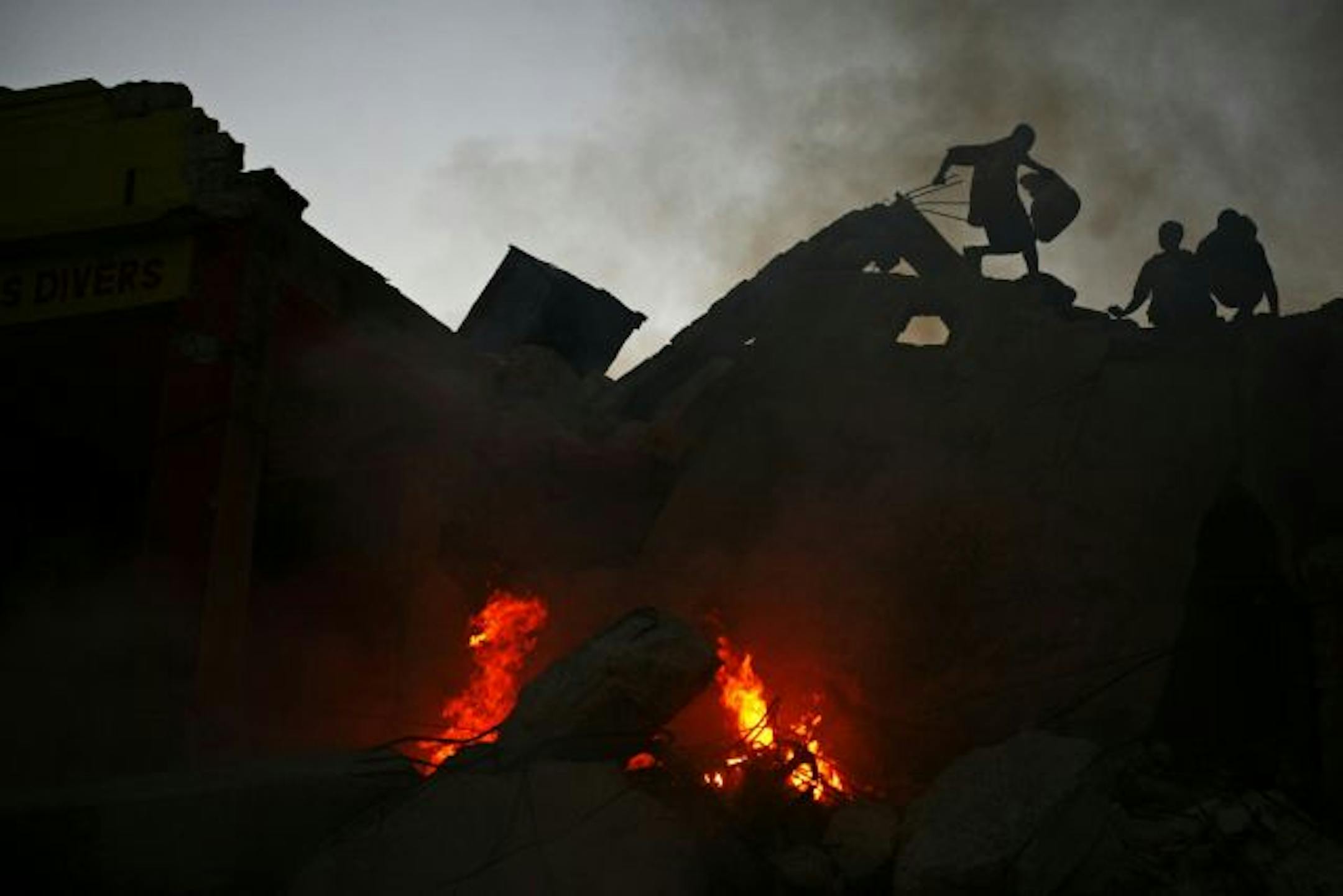 Scavengers walk over the burning rubble of quake-damaged buildings in downtown Port-au-Prince, Haiti.