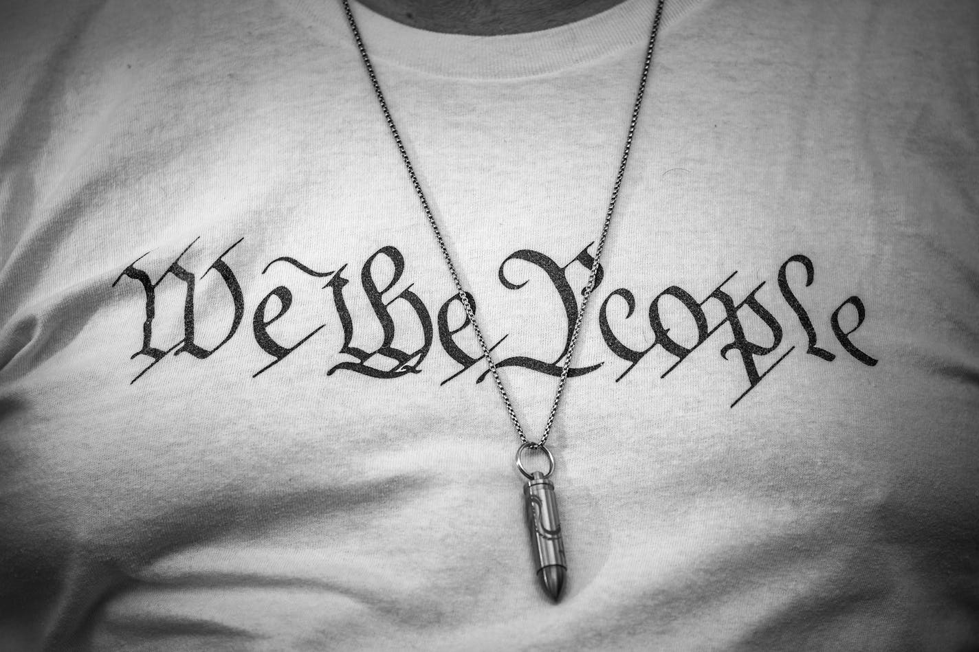 A person wears a bullet necklace over a "We the People" shirt in Miami, Jan. 6, 2022. "You cannot defend the ideal of "E pluribus unum" by deleting pluribus," writes New York Times columnist Bret Stephens. (Damon Winter/The New York Times)