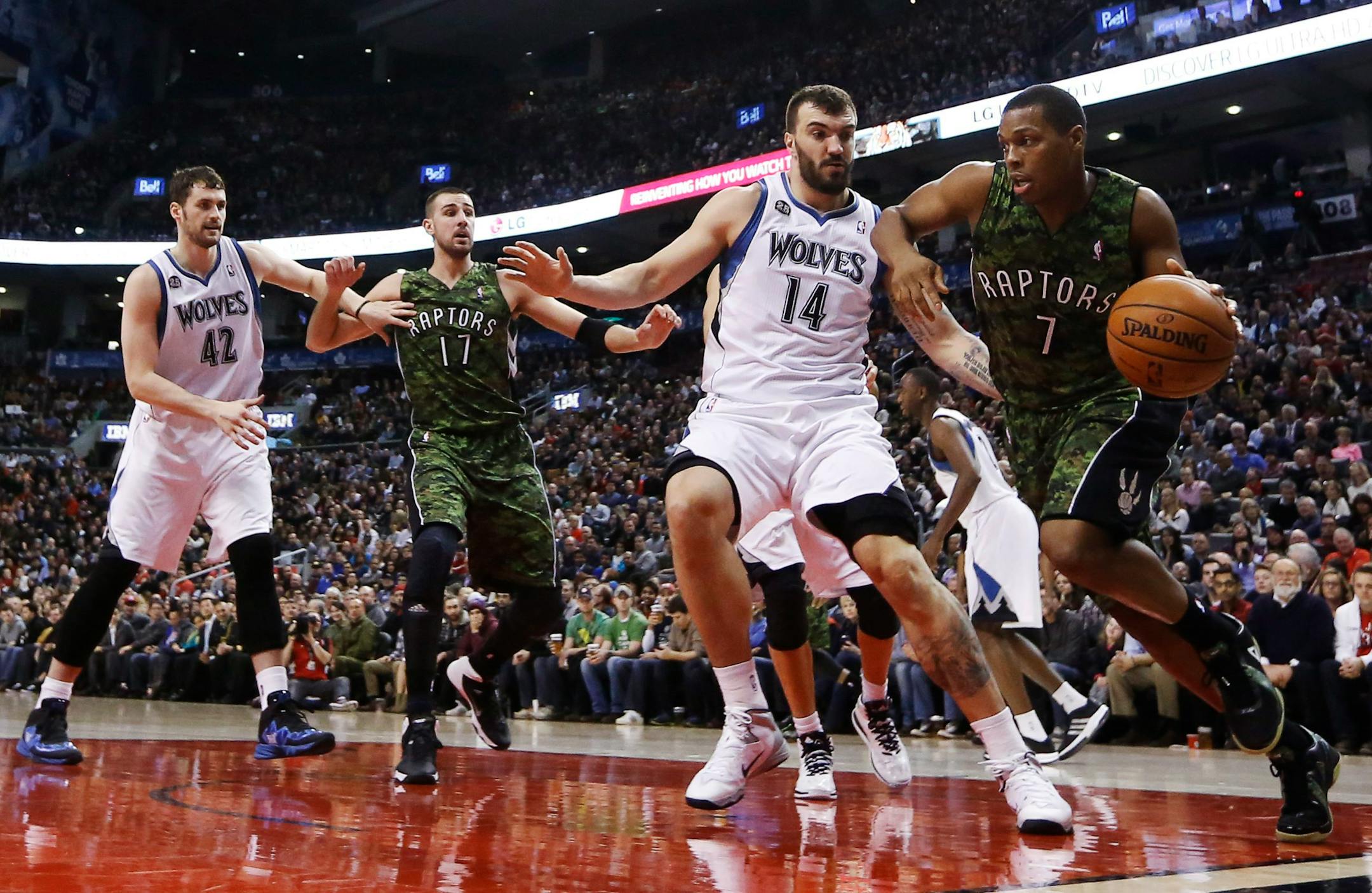Toronto Raptors' Kyle Lowry, right, drives against Minnesota Timberwolves' Nikola Pekovic (14) and Kevin Love (42) during the first half of an NBA basketball game Friday, Jan. 17, 2014, in Toronto. Second from left is Toronto's Jonas Valanciunas. (AP Photo/The Canadian Press, Mark Blinch)