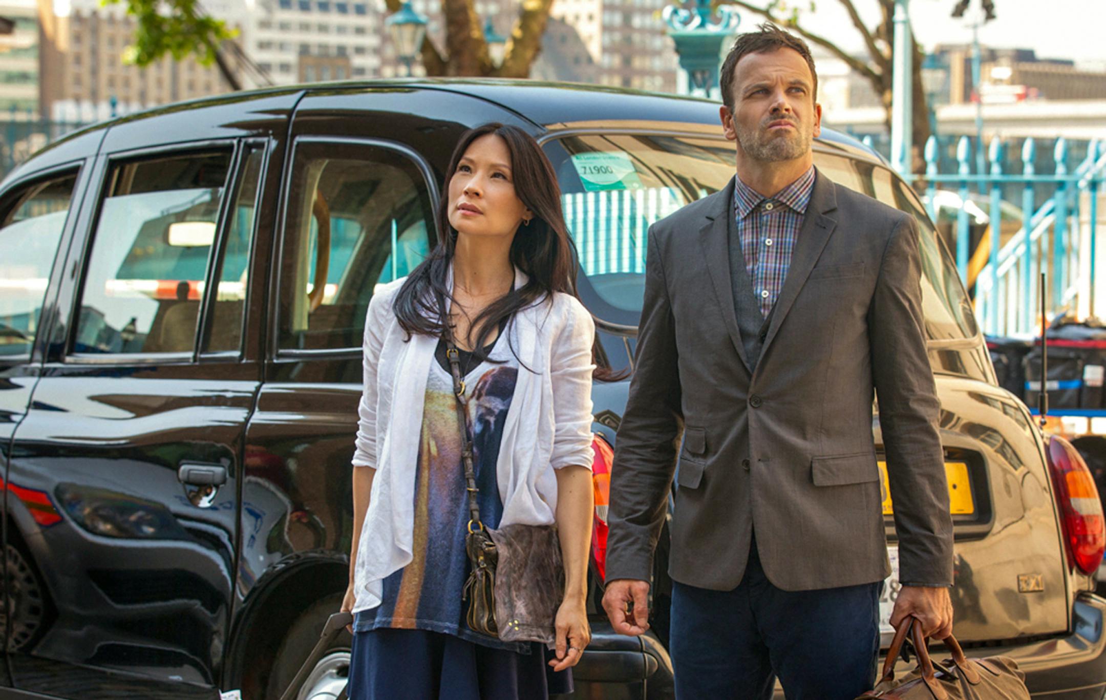 In this undated image image released by CBS Entretainment on Thursday July 13, 2013 Jonny Lee Miller and Lucy Liu are photographed during filming season 2 of "Elementary" on the banks of the Thames in London. Sherlock Holmes is back on home turf in the second-season premiere of "Elementary" _ and so, a bit uncomfortably, is star Jonny Lee Miller."It's a little bit surreal, to be honest with you," said the British actor, who plays a New York-based Sherlock in CBS' modern-day take on the great det