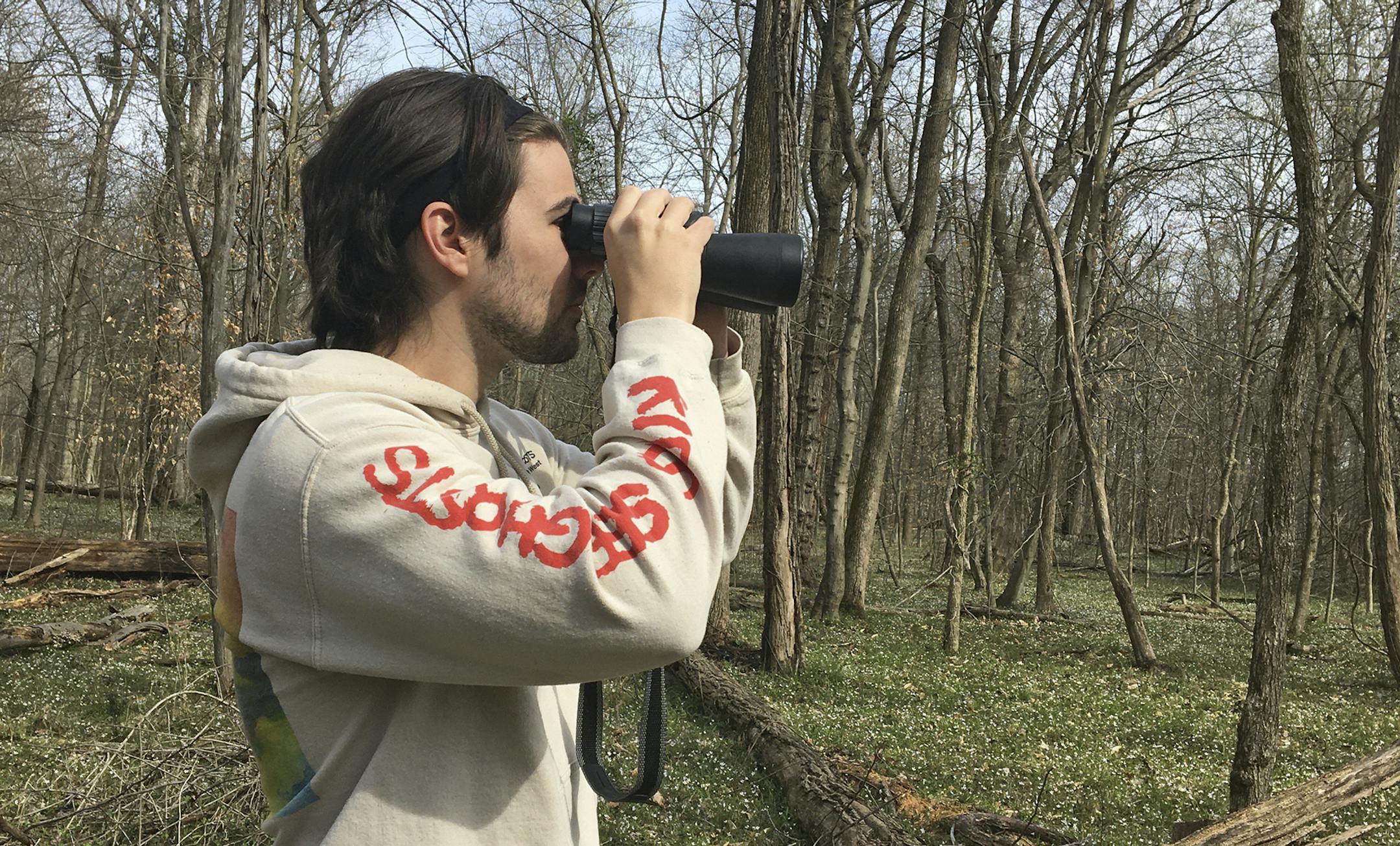 In this March 24, 2020 photo, provided by Conner Brown, he is seen using binoculars to look for birds in Cedar Island, Maryland. Brown, a 25-year-old law school student and Bitcoin aficionado, spent the early days of his coronavirus quarantine following his brother around on long walks as he hunted down and collected characters in a virtual reality video game called Pokemon Go. (Elizabeth Wright/Courtesy of Conner Brown via AP)