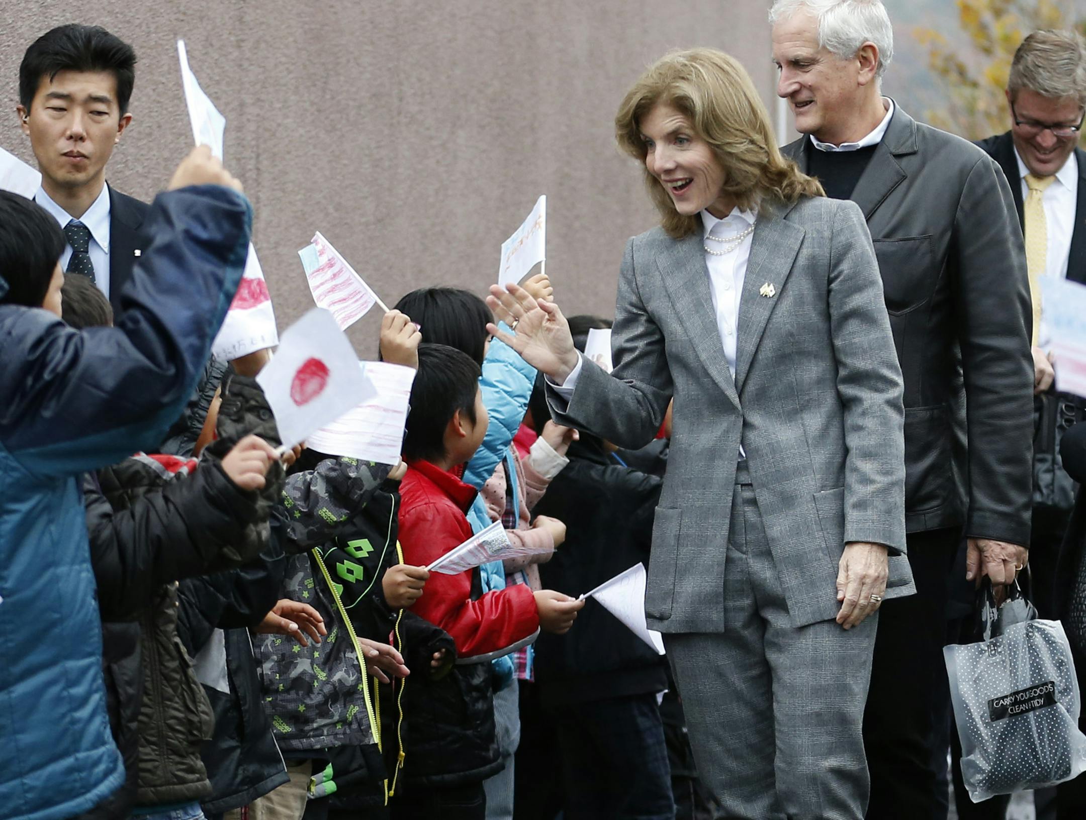 New U.S. Ambassador to Japan Caroline Kennedy, accompanied by her husband Edwin Schlossberg, smiles and waves at schoolchildren greeted her with the U.S. and Japanese flags upon her arrival at Mangokuura Elementary School in Ishinomaki, Miyagi Prefecture, northeastern Japan, Monday, Nov. 25, 2013. Kennedy, who arrived in Japan on Nov. 15, practiced calligraphy, exchanged high-fives with schoolchildren and got an early birthday present as she toured areas in northeastern Japan devastated by the M