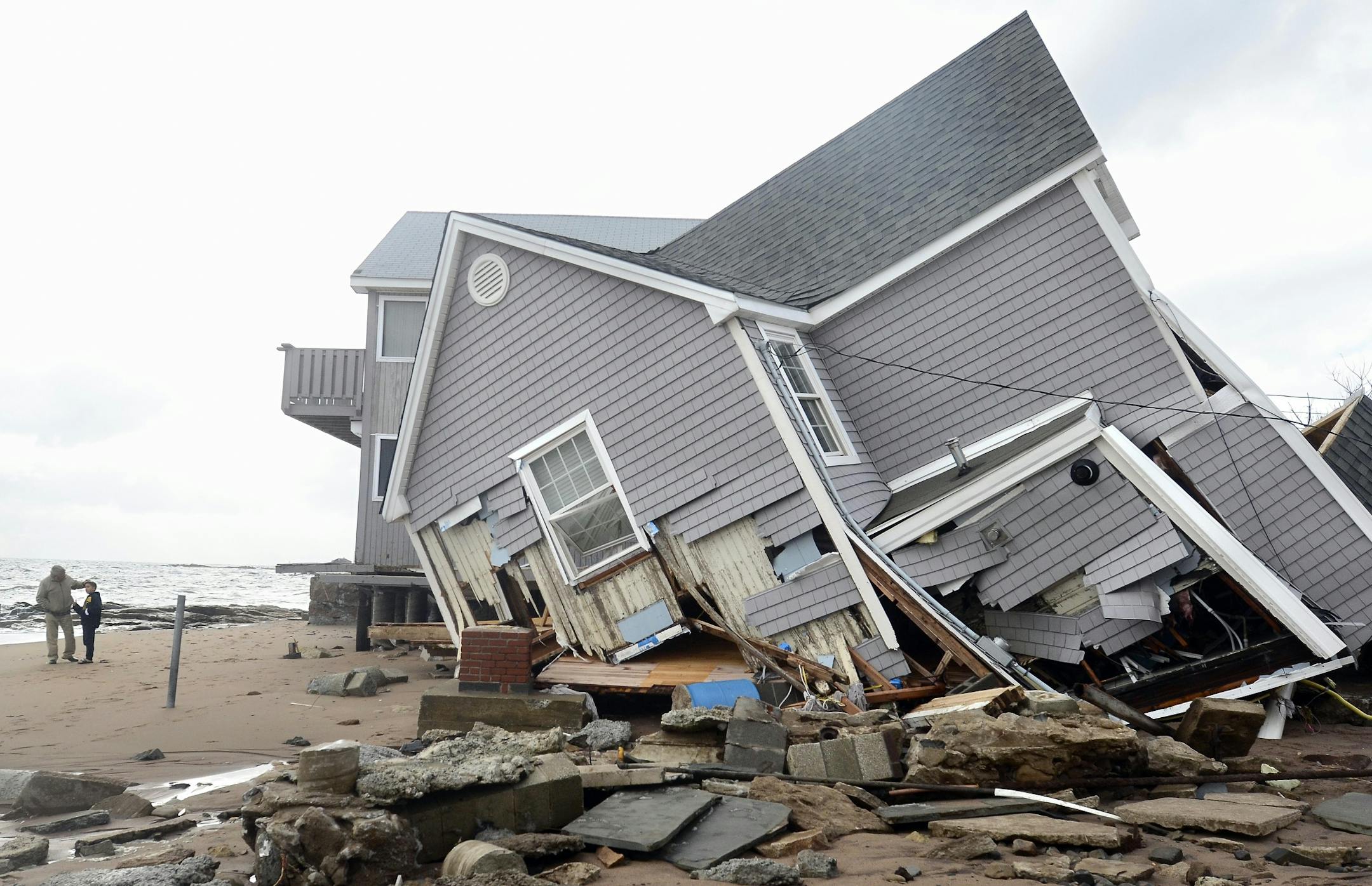 People stand next to a house collapsed from superstorm Sandy in East Haven, Conn. on Tuesday, Oct. 30, 2012.