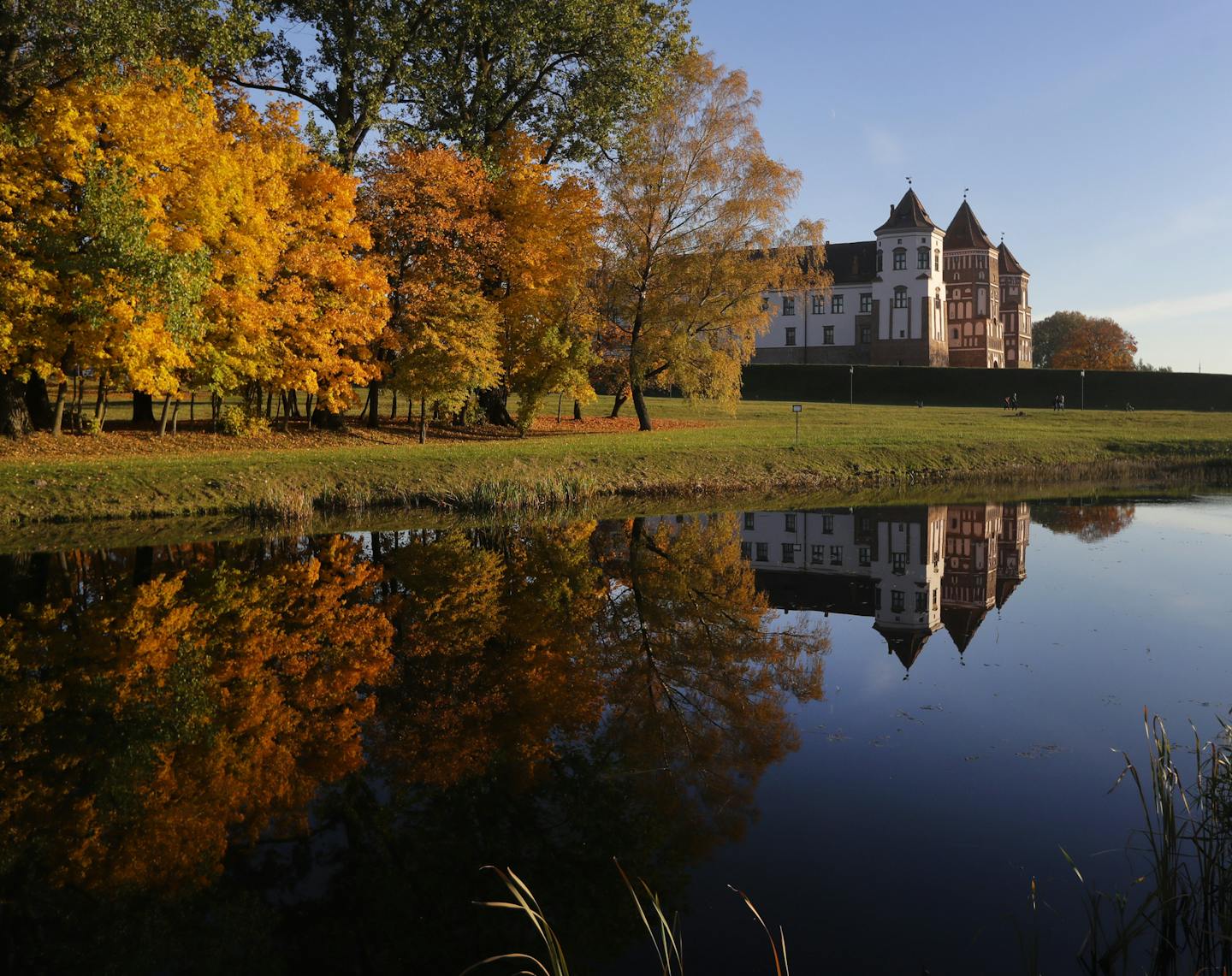 People walks next to a medieval castle among seasonal coloured trees on an autumn day in Mir, Belarus, 95 kilometers (60 miles) west of Minsk, Sunday, Oct. 14, 2018. (AP Photo/Sergei Grits) ORG XMIT: XSG101