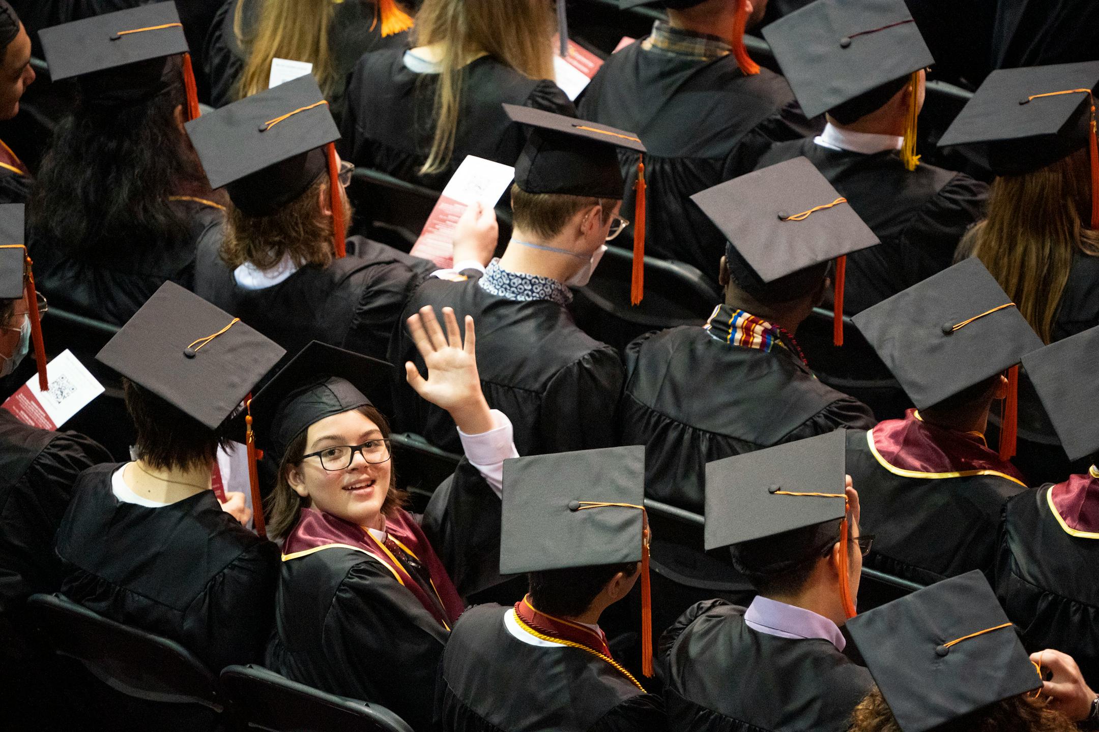 Elliott Tanner, 13, waves to his parents in the stands while sitting among his fellow physics department graduates during his graduation.