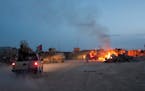 An Afghan National Army pickup truck passes parked U.S. armored military vehicles as smoke rises from a fire in a burn pit at Forward Operating Base C