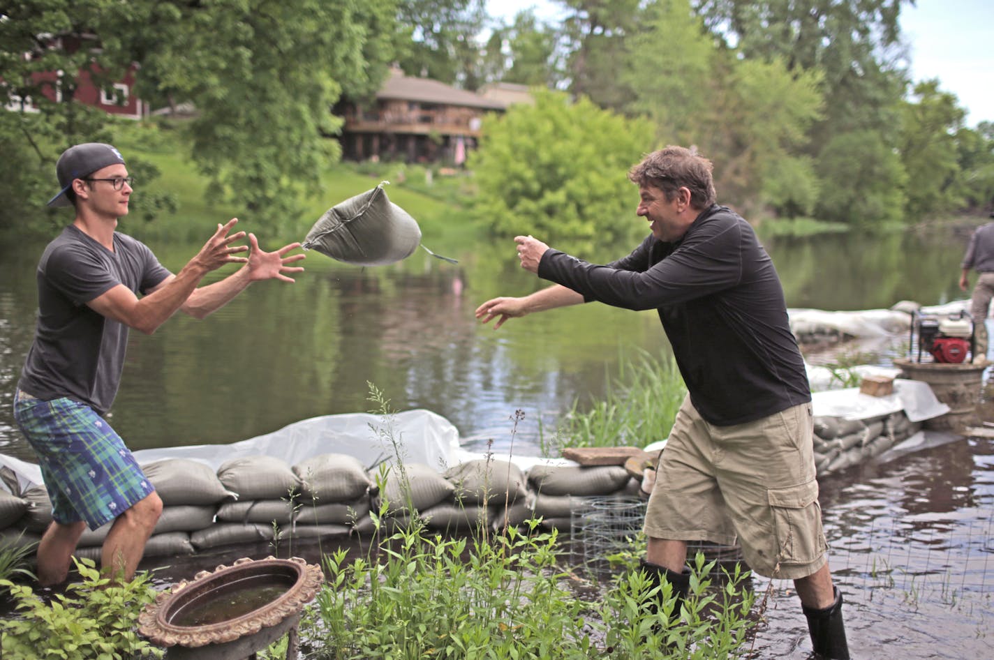 Marshall Rosner, center, tosses a sandbag to Chase Gross in the Gross family backyard on Cascade Lane along Minnehaha Creek Sunday afternoon as neighbor helped neighbor sandbag against the flooded creek. The neighbors had spent the day helping one another sandbag homes on the cul-de-sac. Far in background is neighbor Gary Aulik, also a neighbor. ] David Denney - Star Tribune 6/1/2014 Edina, MN