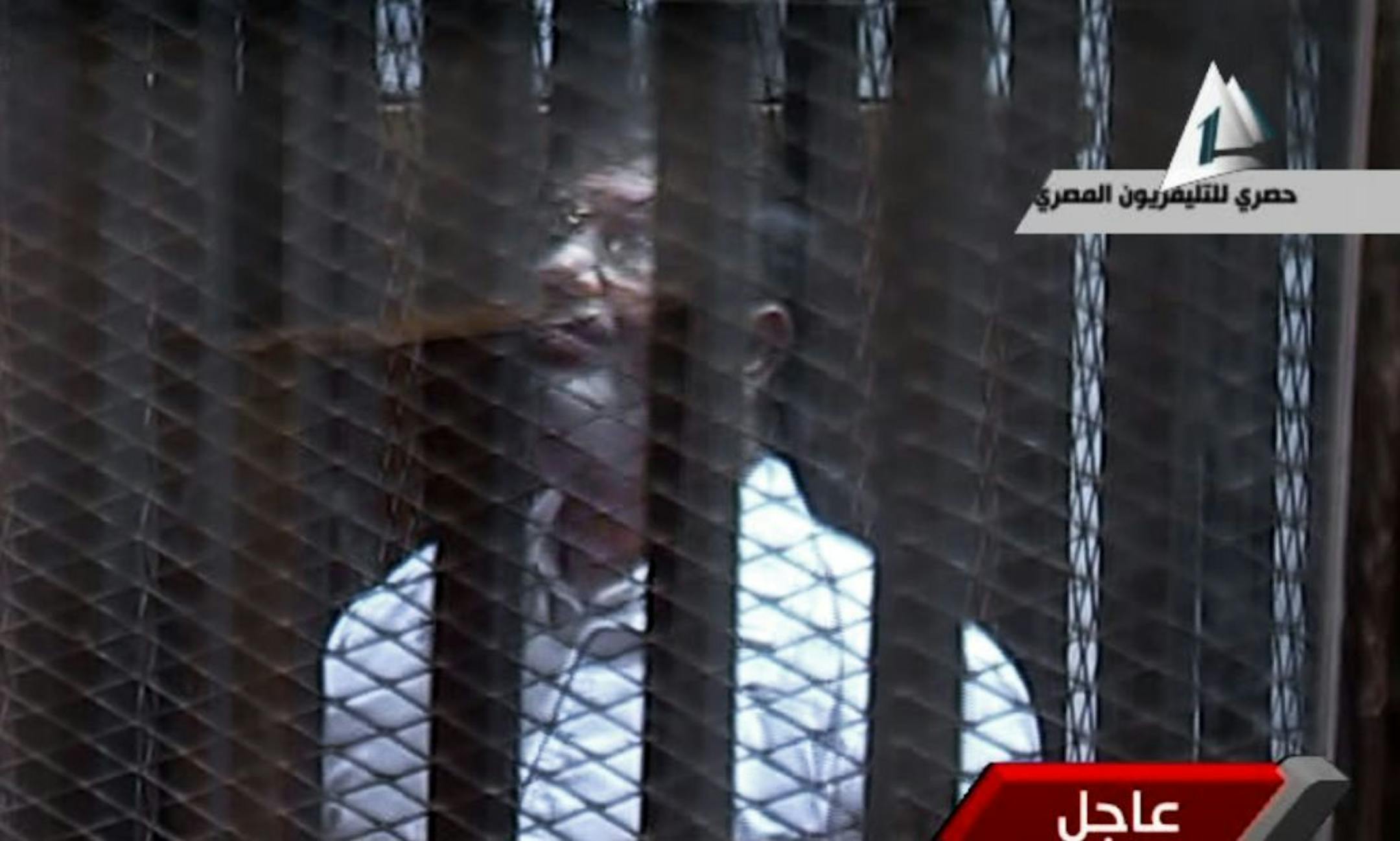 In this image taken from Egypt State TV, Egypt's toppled President Mohammed Morsi stands inside a glass-encased metal cage in a courtroom in Cairo, Egypt, Tuesday, Jan. 28. 2014.