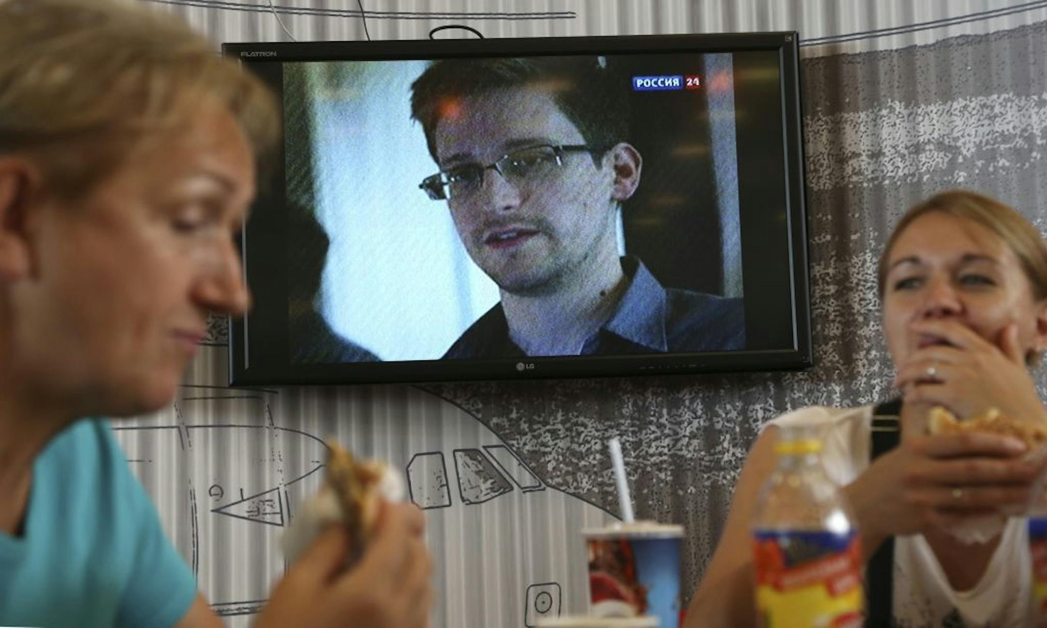 Transit passengers eat at a cafe with a TV screen with a news program showing a report on Edward Snowden, in the background, at Sheremetyevo airport in Moscow Wednesday, June 26, 2013. Russia�s President Vladimir Putin said Tuesday that National Security Agency leaker Edward Snowden has remained in Sheremetyevo�s transit zone, but media that descended on the airport in the search for him couldn�t locate him there.