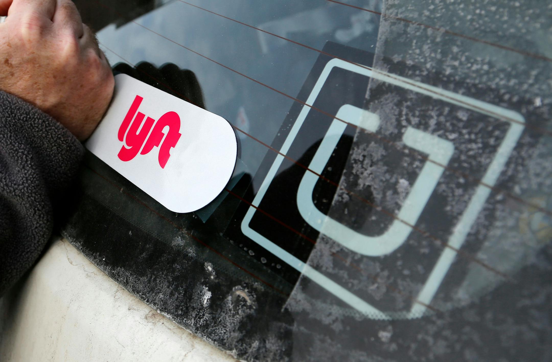 FILE- In this Jan. 31, 2018, file photo, a Lyft logo is installed on a Lyft driver's car next to an Uber sticker in Pittsburgh. Uber and Lyft drivers might seem well-insured, between the ride-booking companiesí coverage and their own policies. However, a crucial gap leaves drivers at risk if they have an accident at the wrong time. (AP Photo/Gene J. Puskar, File)