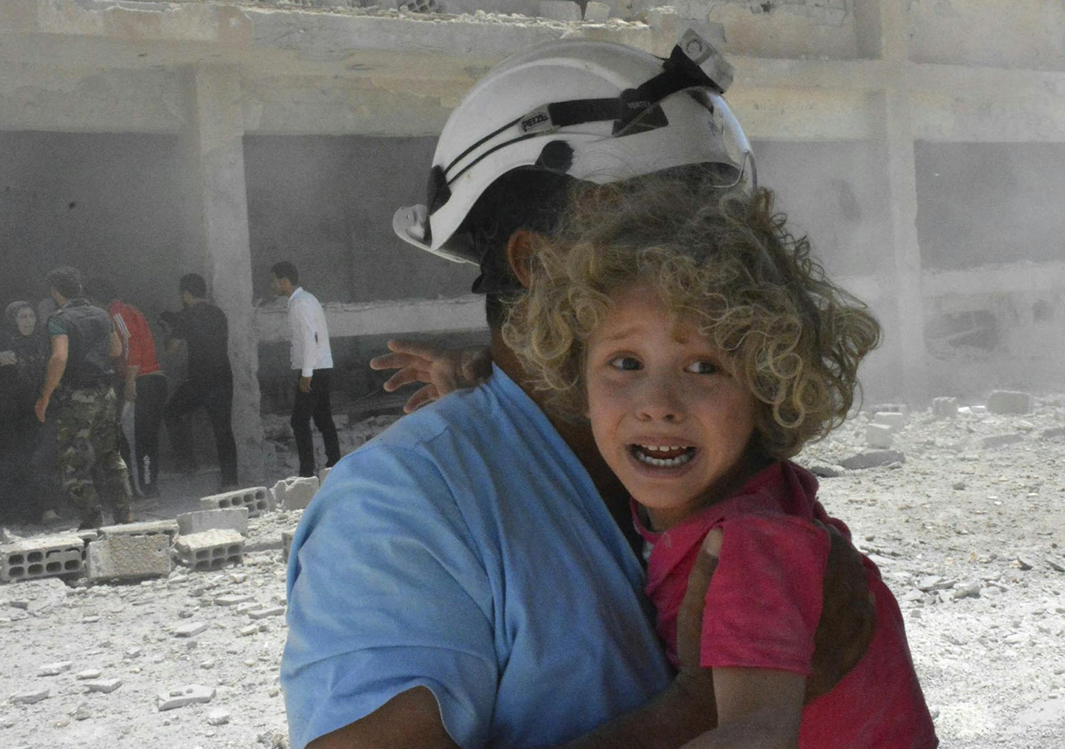 This photo provided by the Syrian Civil Defense group known as the White Helmets, shows a civil defense worker carrying a child after airstrikes hit a school housing a number of displaced people, in the western part of the southern Daraa province of Syria, Wednesday, June 14, 2017. A U.N. investigative commission said Wednesday that the "de-escalation" agreement in Syria has reduced violence in only one of four zones included in the deal and has not led to greater humanitarian access. (Syrian Ci