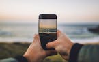 Two hands taking a picture with a mobile phone of a beach at sunset. istock