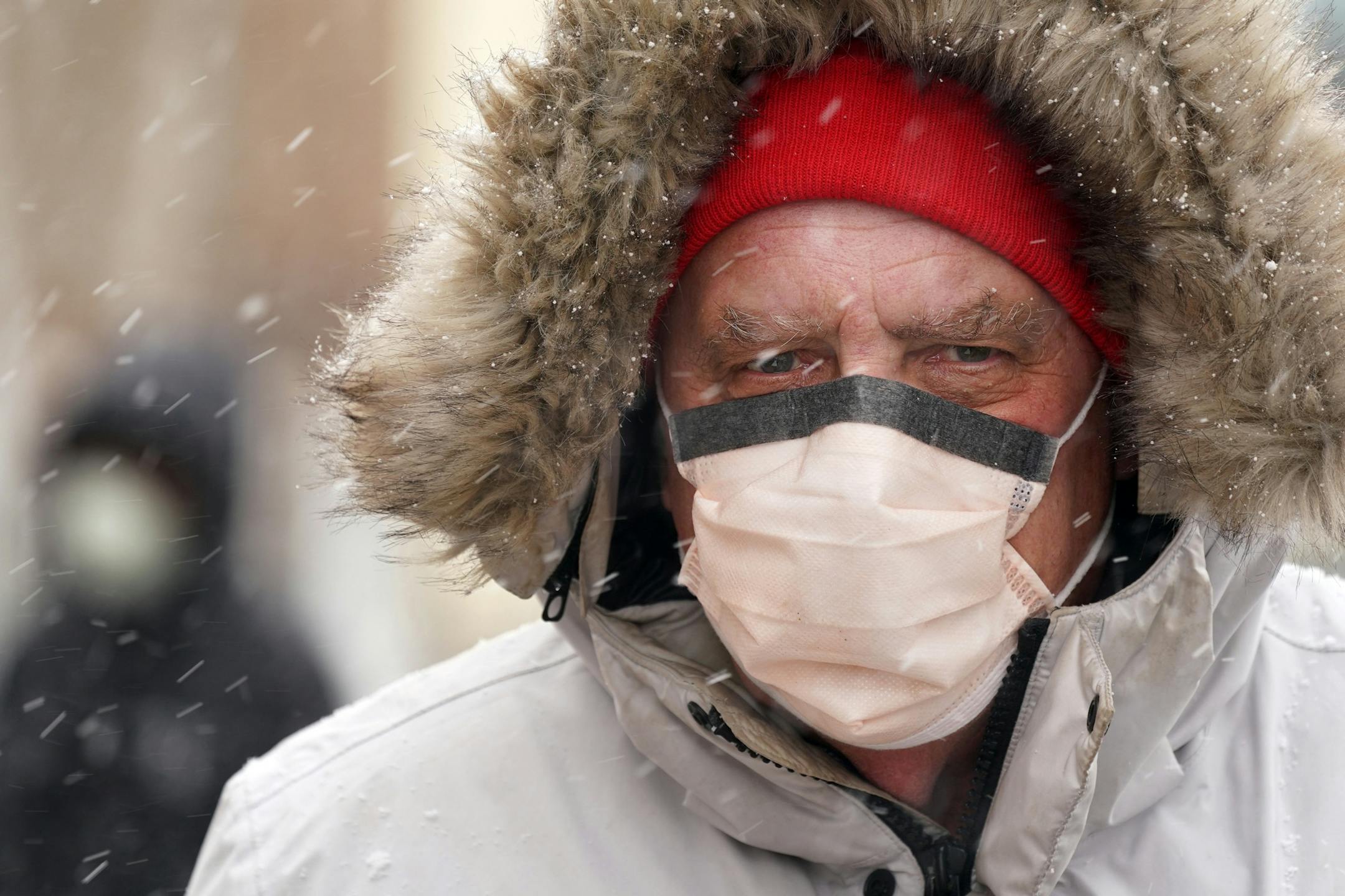 Larry Utterback of Minneapolis wore both a winter coat to protect himself from the cold and a surgical mask to protect himself from Coronavirus as a sudden burst of snow fell on the Ventura Village neighbored Tuesday afternoon.