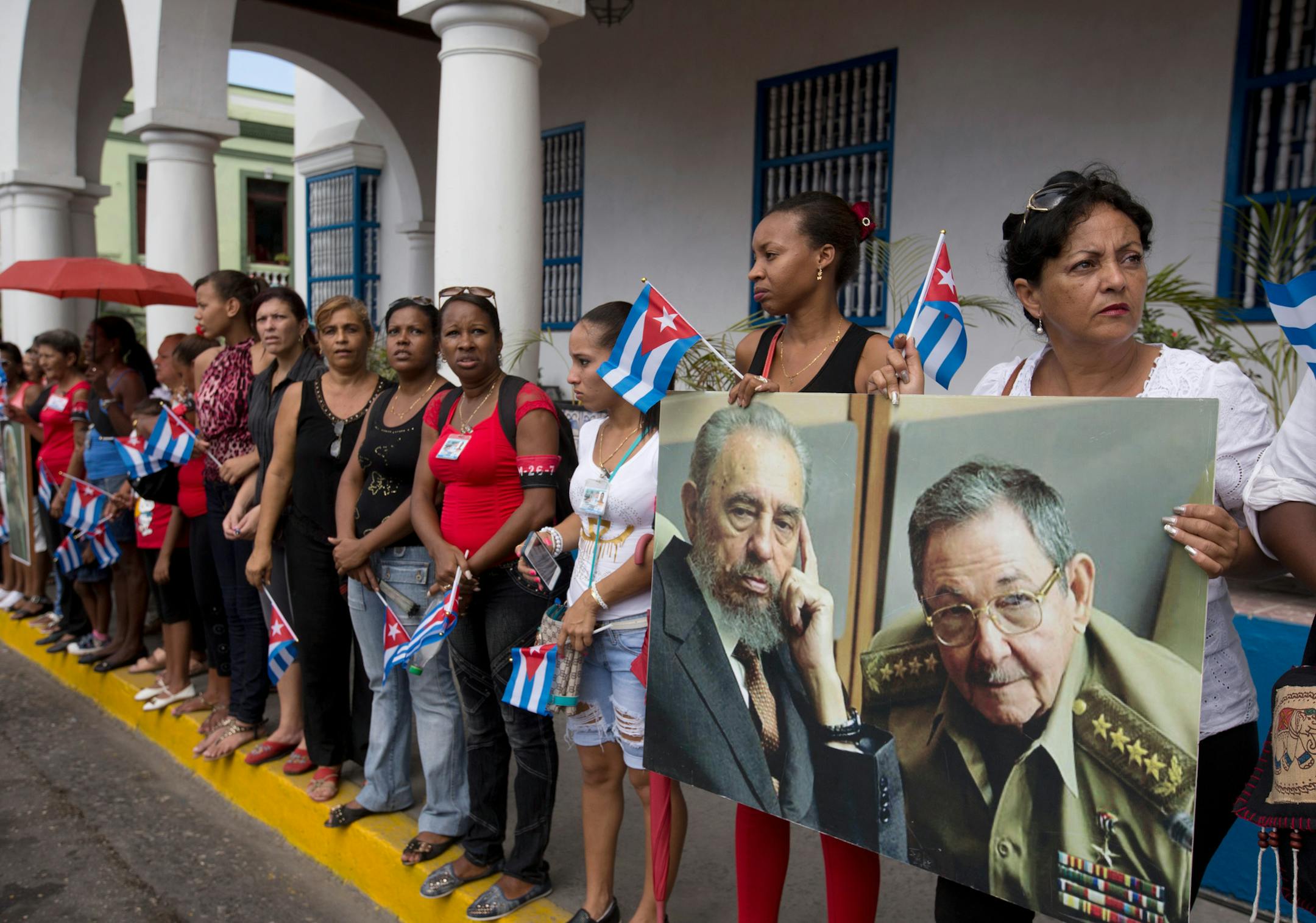FILE - In this Dec. 3, 2016 file photo, women hold a portrait of the late Fidel Castro, and of his brother Cuba's President Raul Castro, as they wait to see the arrival of the caravan transporting Fidel's ashes from Havana, in Santiago, Cuba. The caravan was fraught with symbolism as the island nation buried the only leader it had known besides his younger brother, Raul, in 57 years. (AP Photo/Ricardo Mazalan, File)