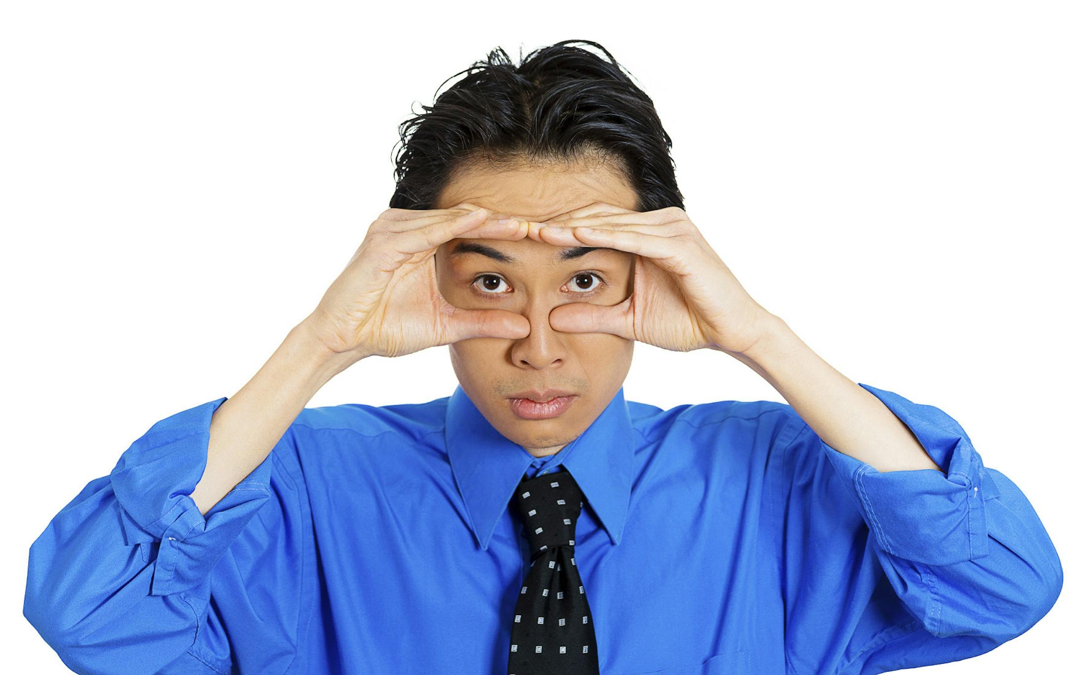 Closeup portrait of a young serious curious man peeking through his fingers like binoculars, searching for something, looking to the future at the camera, isolated on a white background. Sign, symbols