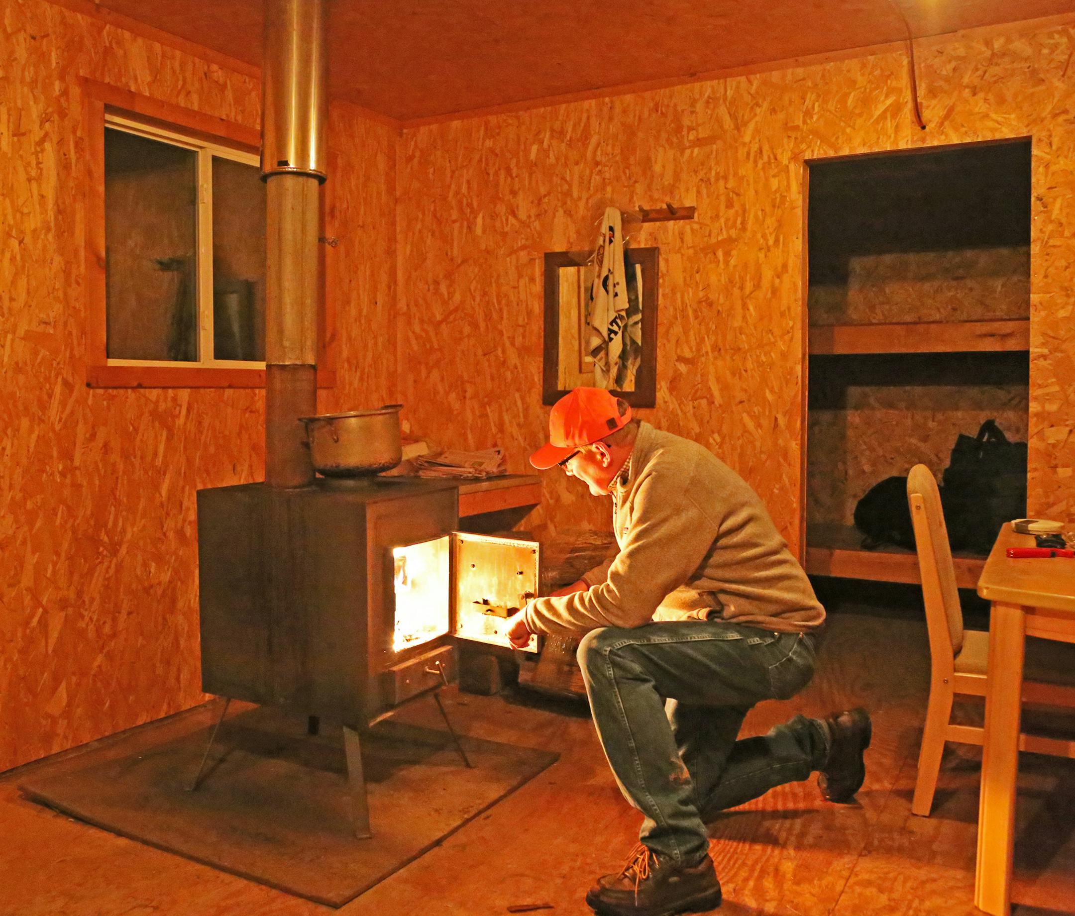 STOKING THE FIRE: After dinner, the group departs to various barns and shacks, hoping for sleep before rising early Saturday to hunt. Here Dennis Anderson fires up a wood stove upon arrival after dinner at a shack on the Berg property where he headquarters during the Wisconsin season.