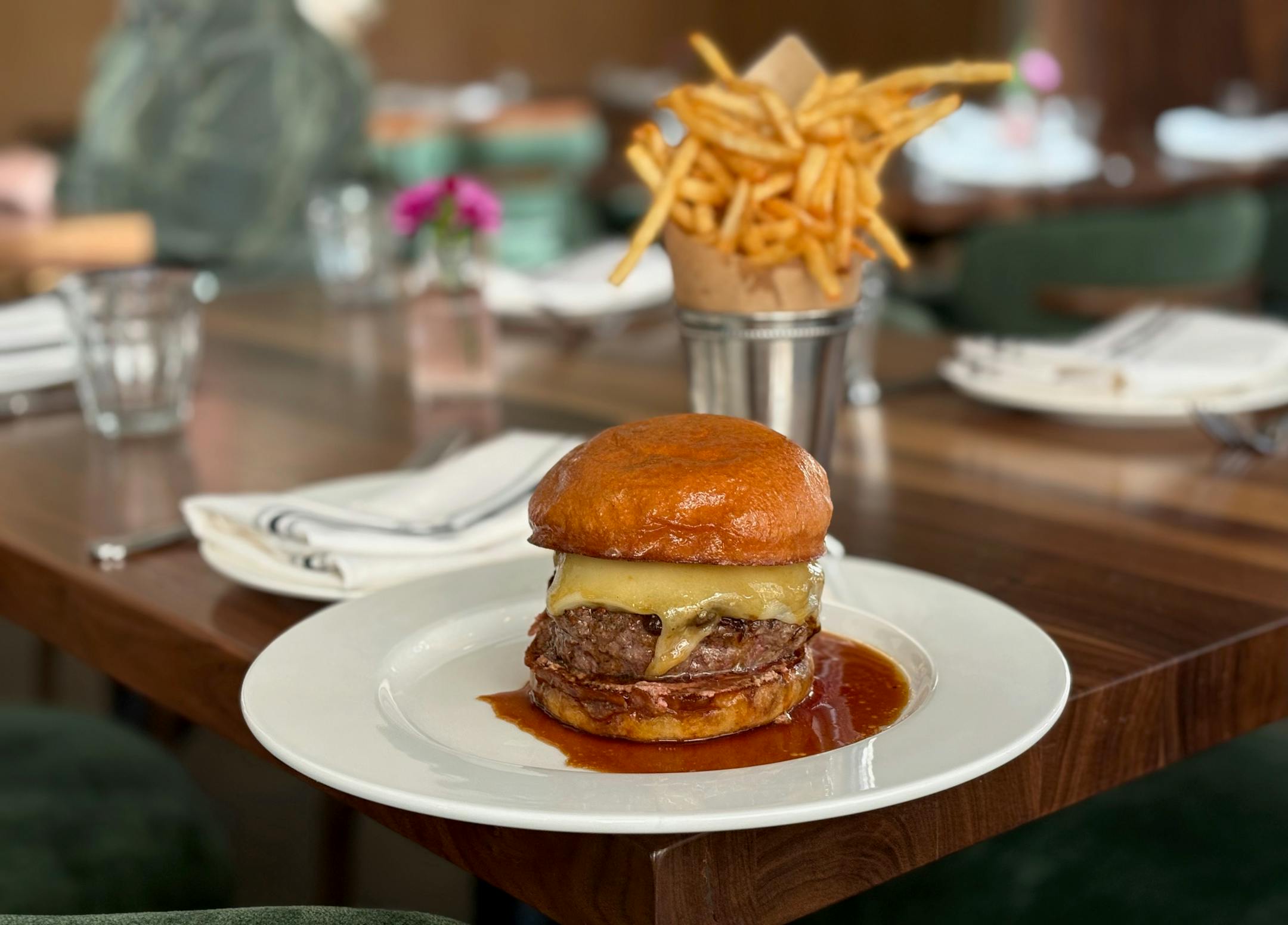 The burger on a white plate with a pool of dark juice and fries in the background.