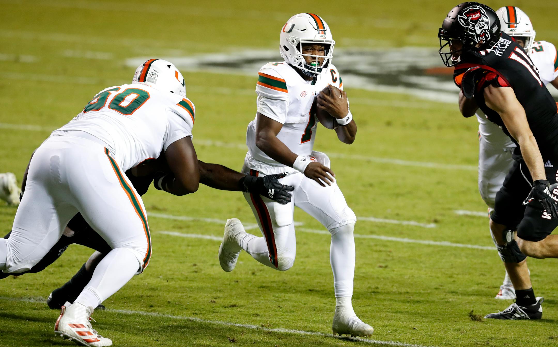 Miami quarterback D'Eriq King runs past North Carolina State linebacker Isaiah Moore, obscured at left, during the first half