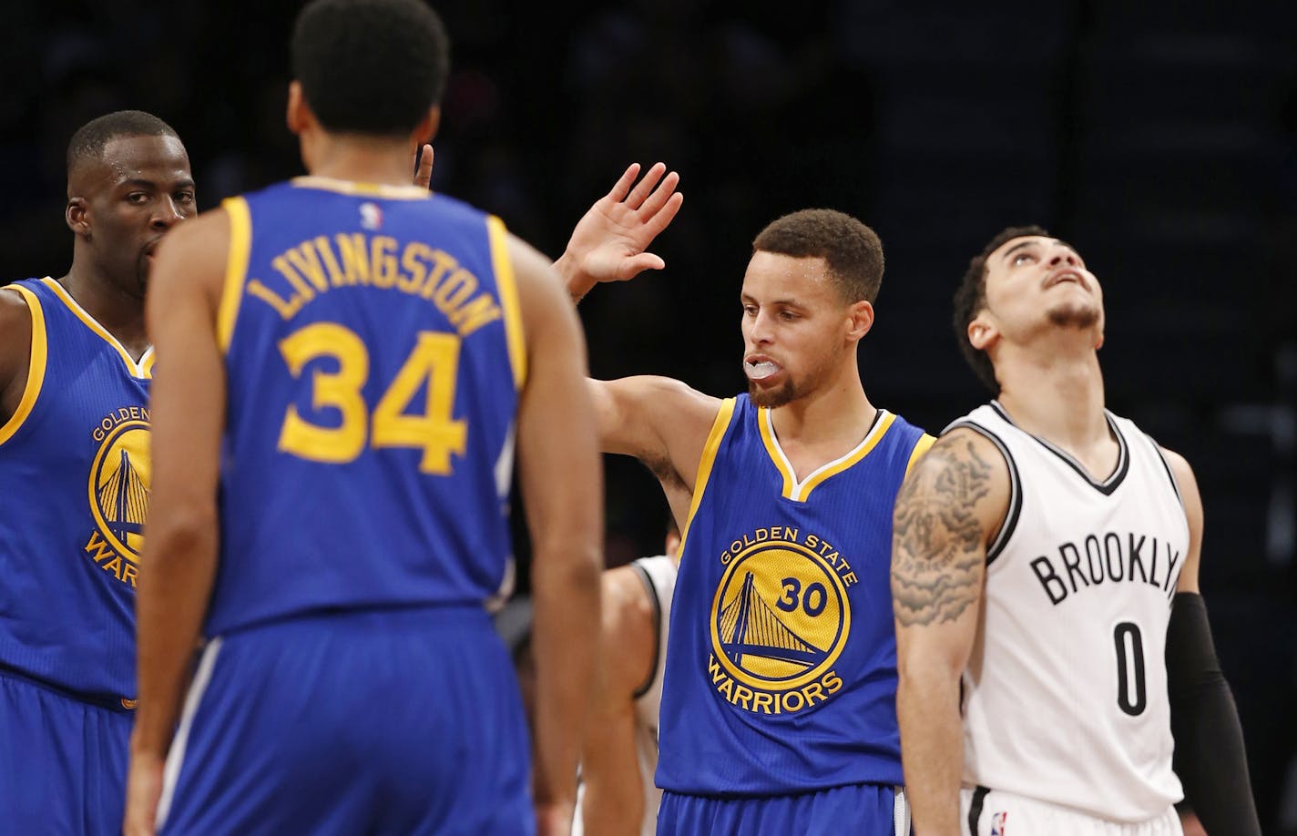 Golden State Warriors guard Stephen Curry (30) celebrates with teammates Andre Iguodala, far left, and Shaun Livingston (34) as Brooklyn Nets guard Shane Larkin (0) looks at a replay on screen overhead in the second half of an NBA basketball game, Sunday, Dec. 6, 2015, in New York. The Warriors defeated the Nets 114-98, extending their winning streak to 22. (AP Photo/Kathy Willens)