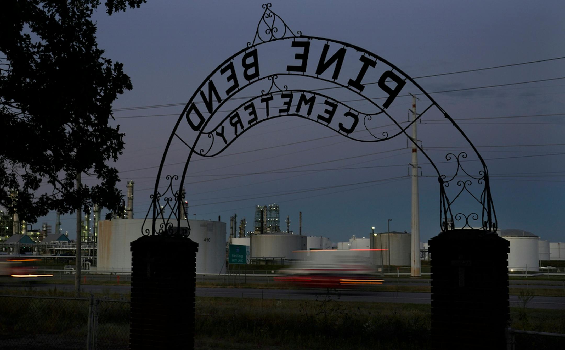 The Pine Bend Cemetery entrance sign frames nearby Pine Bend Refinery, owned by Koch Industries, and traffic along Hwy. 52.